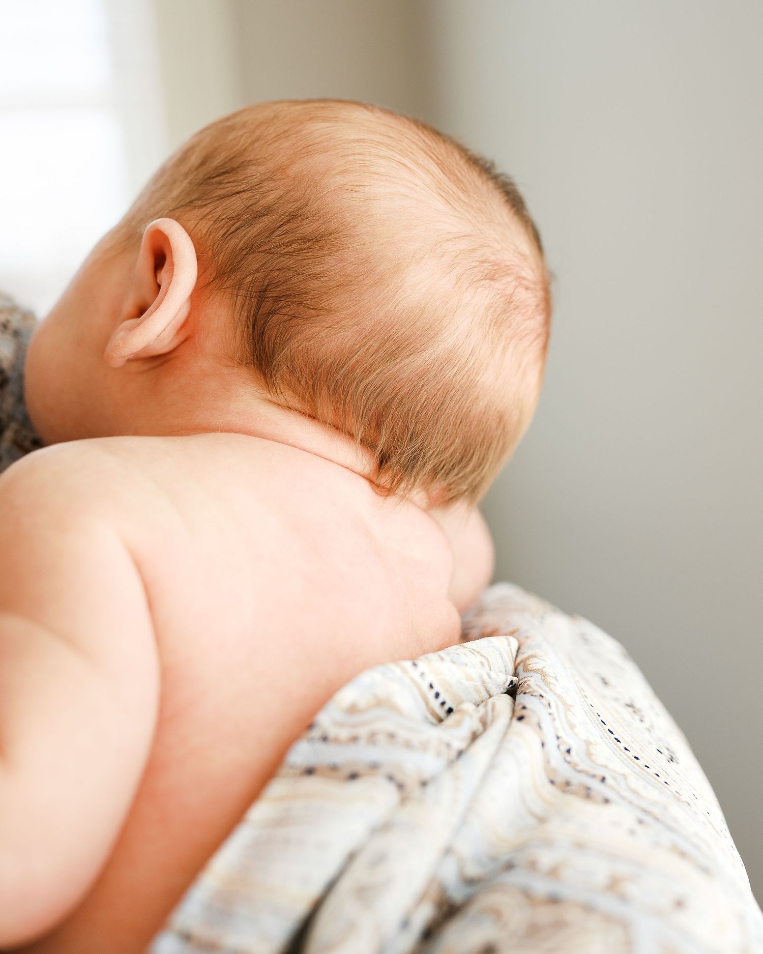 Close-up view of baby's soft head and bare shoulders resting on patterned fabric.
