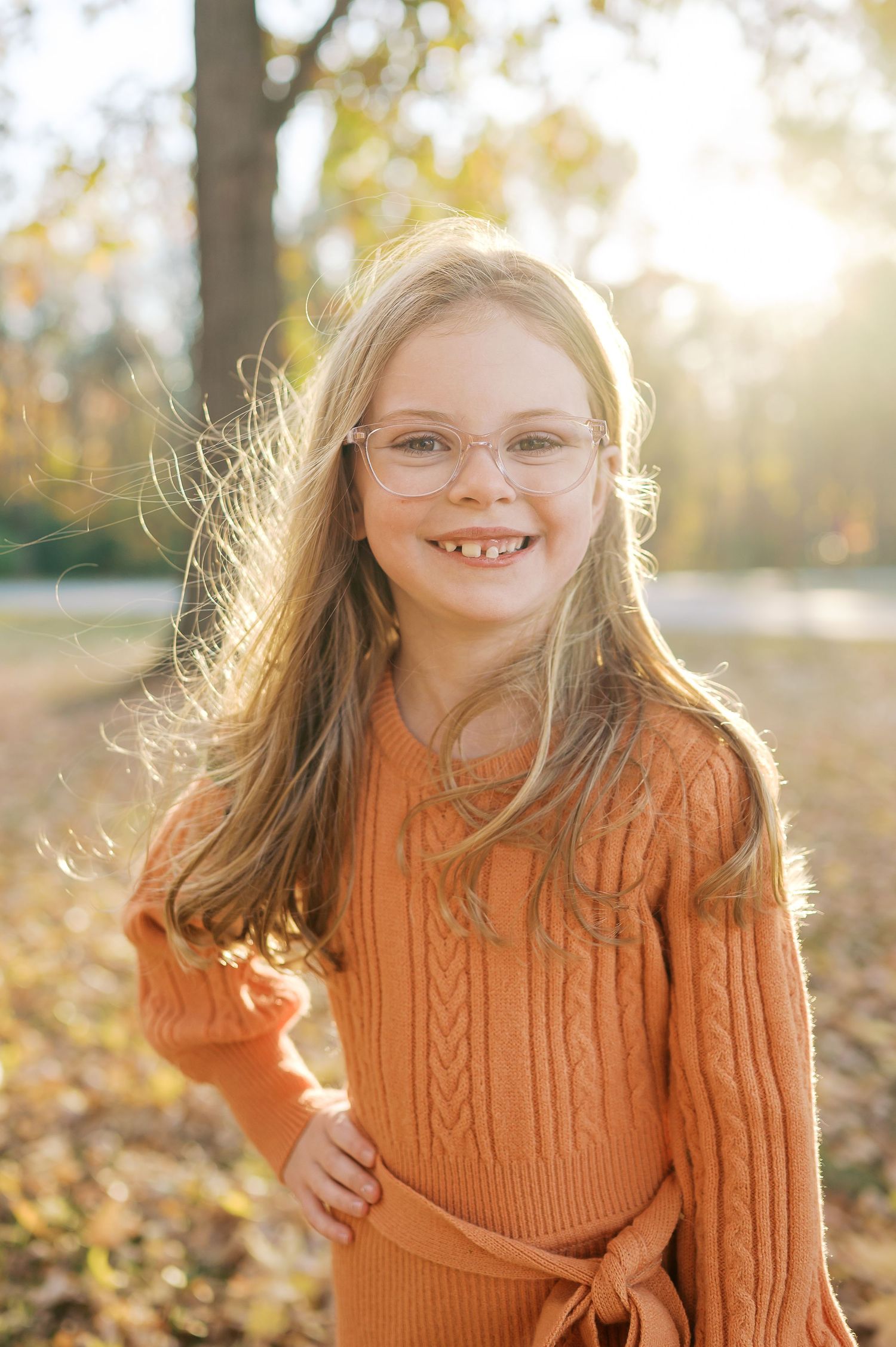 Portrait in warm autumn light wearing an orange cable knit sweater among fall foliage.