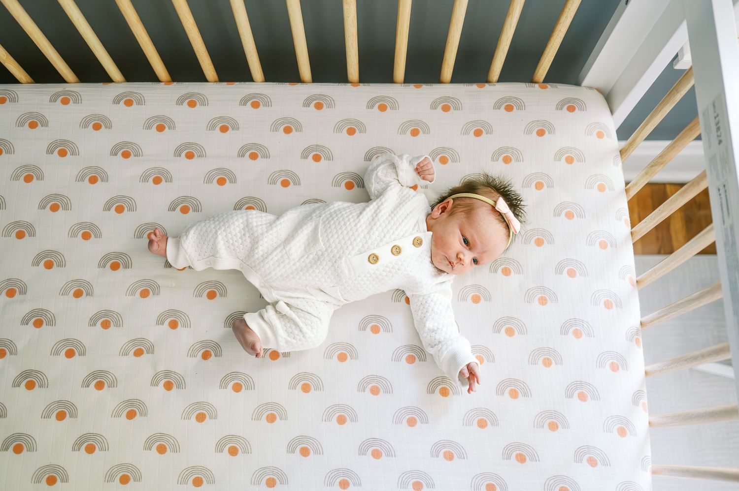 Wide view of wooden crib with rainbow polka dot bedding in nursery.