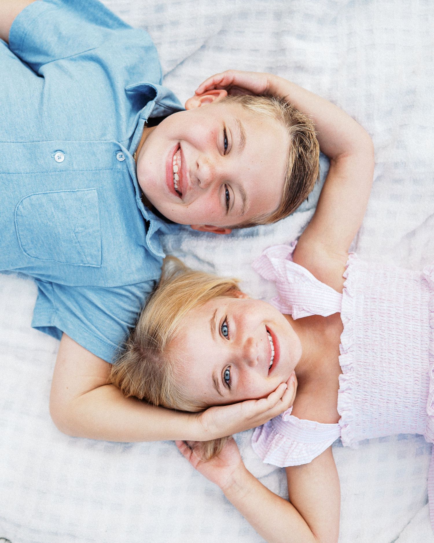 Two children lying on a white blanket sharing a playful moment together.