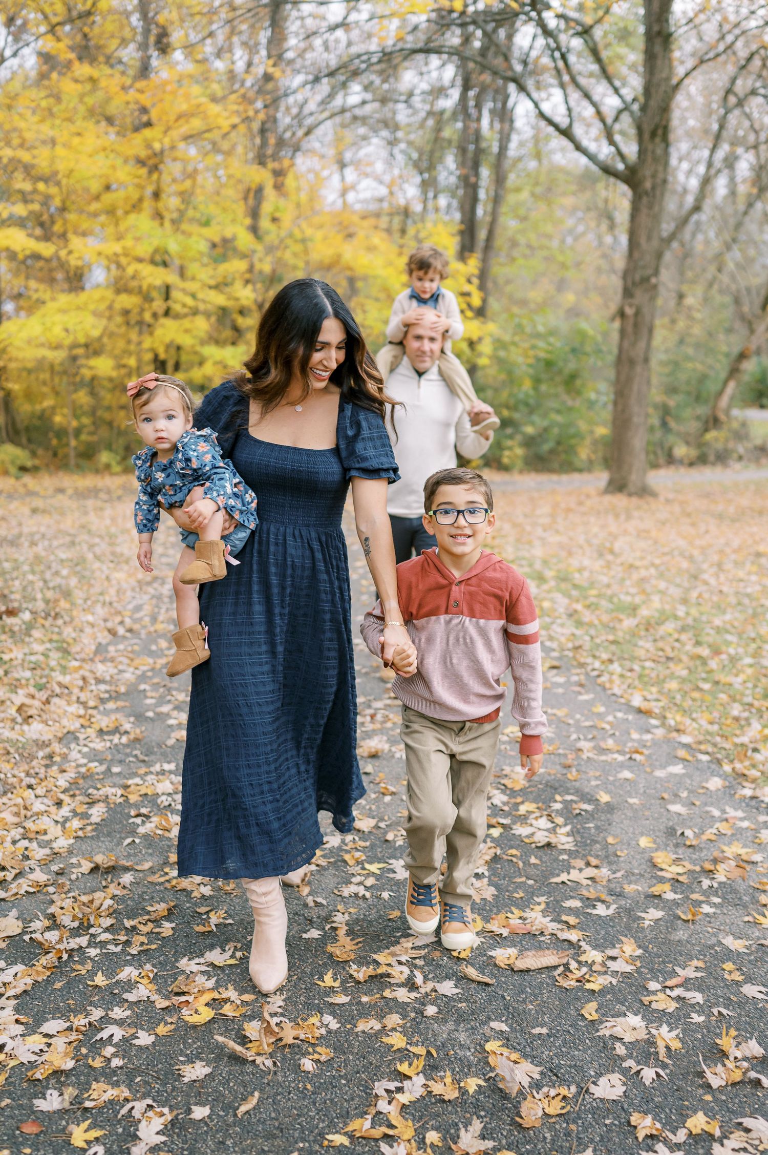 A family takes an autumn stroll down a leaf-covered path surrounded by golden foliage in a park.