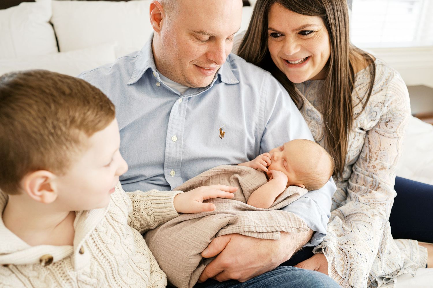 A family sits together on a couch while tenderly gazing at their newborn baby.