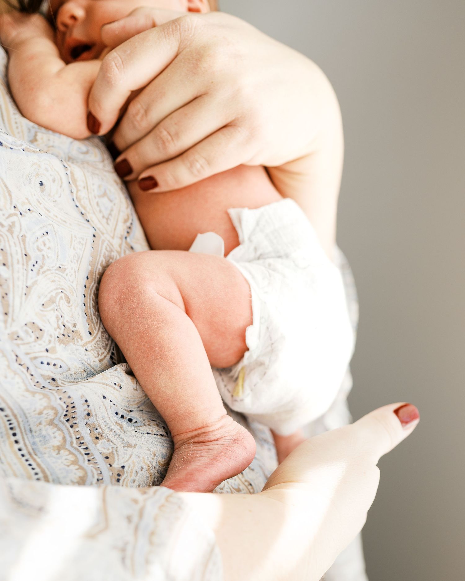 Close-up of infant's delicate limbs being held against a patterned white dress.