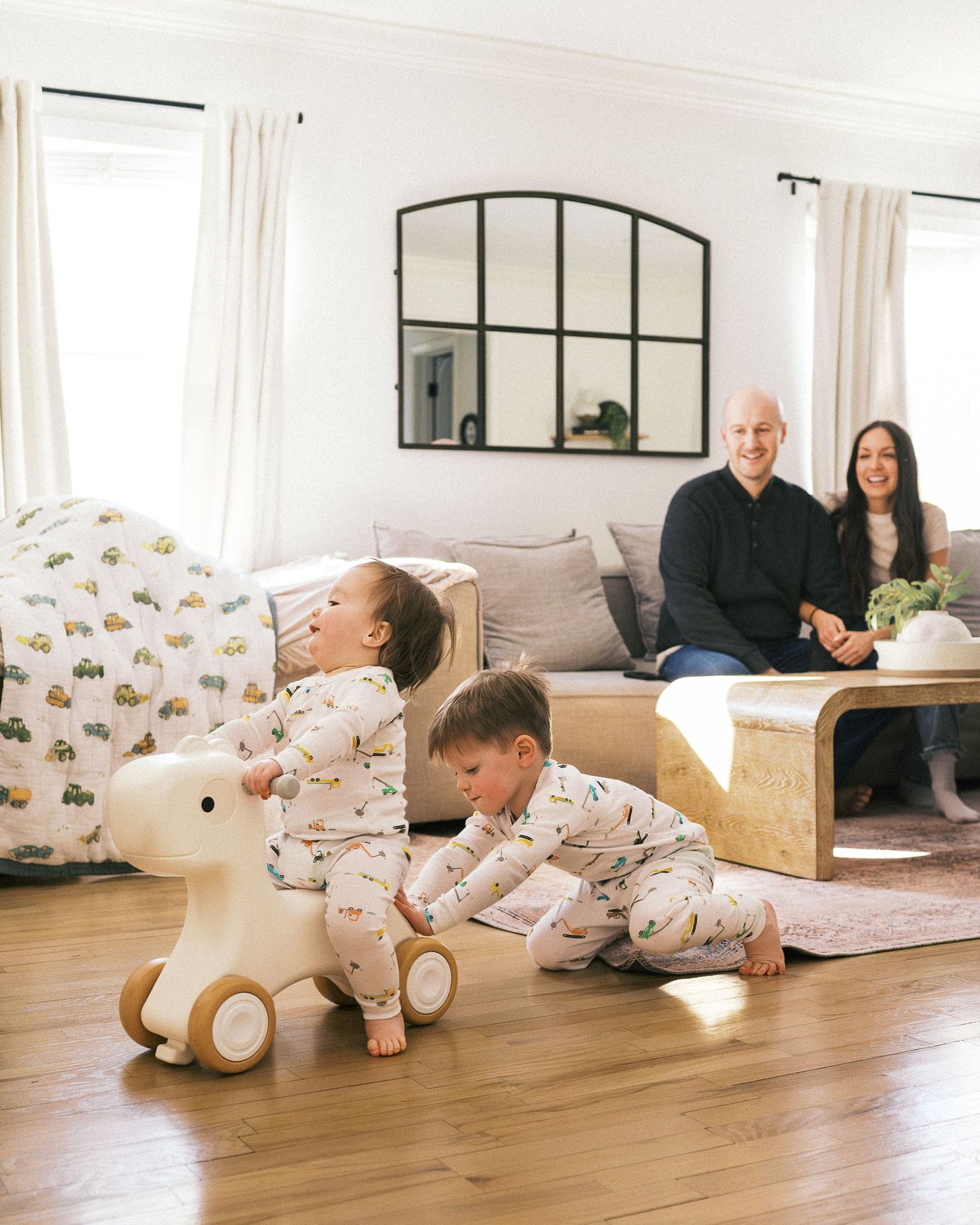 Children playing with wooden ride-on toy in bright living room with modern furniture.