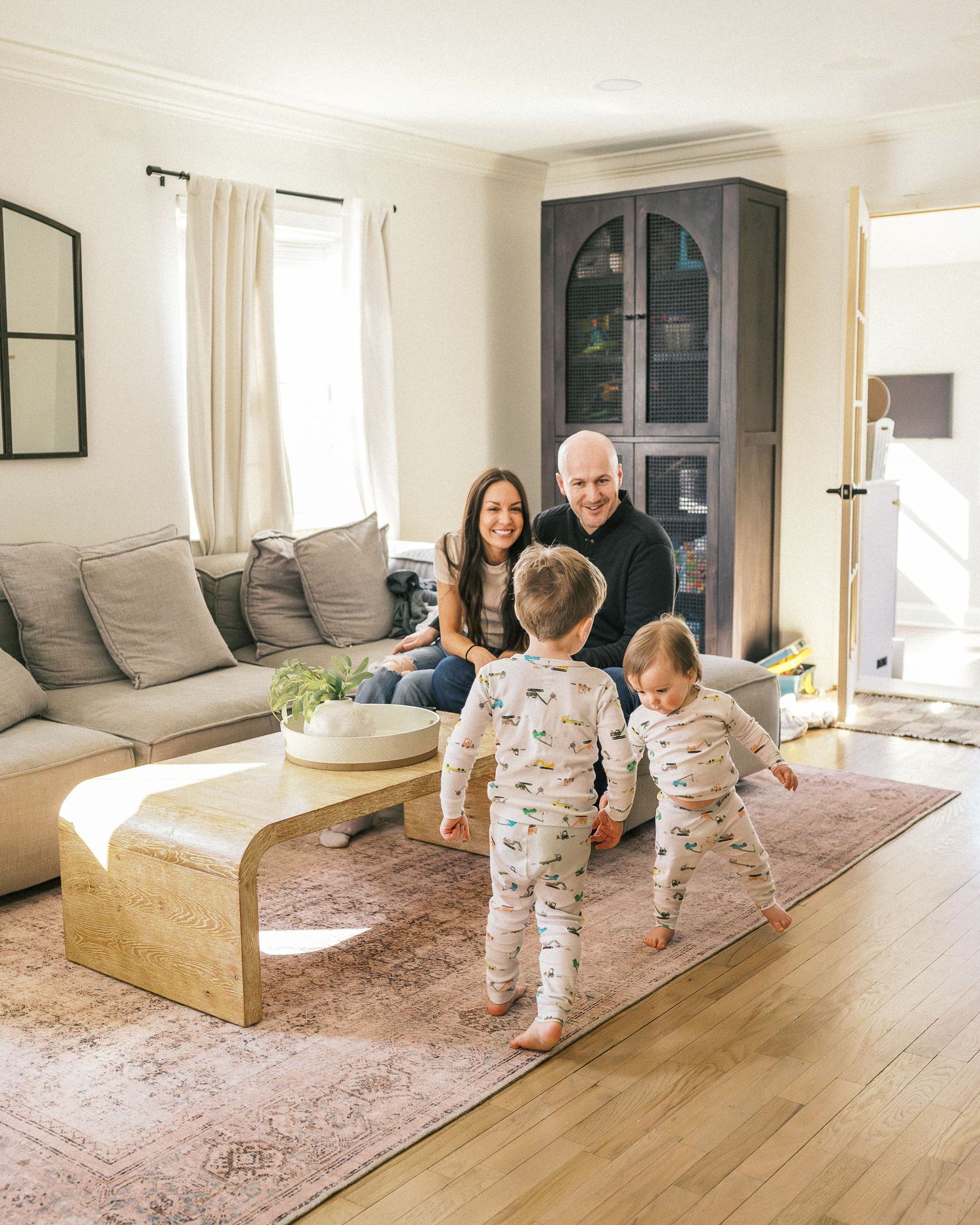 Family enjoys playful moment together in cozy living room with gray couch and arched cabinet.