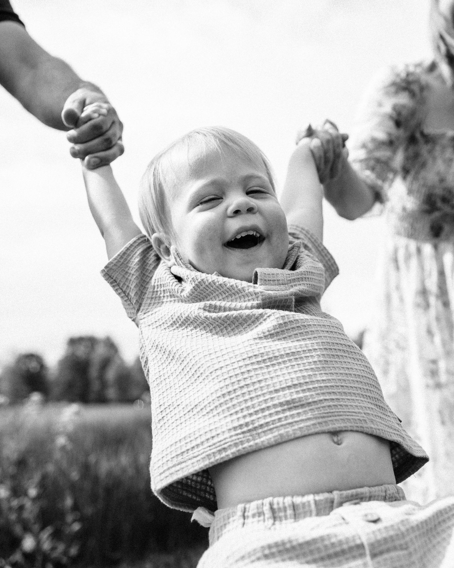 Black and white series of joyful baby wearing checkered shirt playing outdoors.