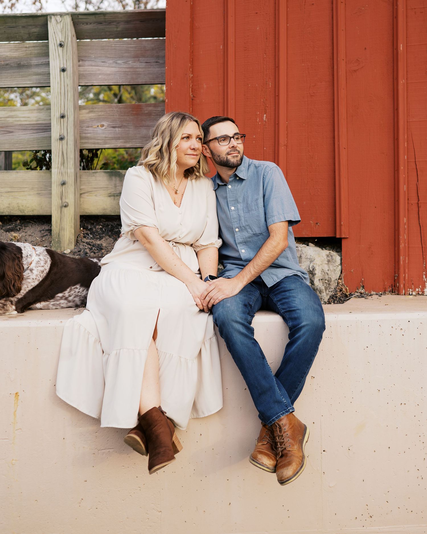 A couple sits together on a wooden deck against a rustic red barn wall during a photo session.