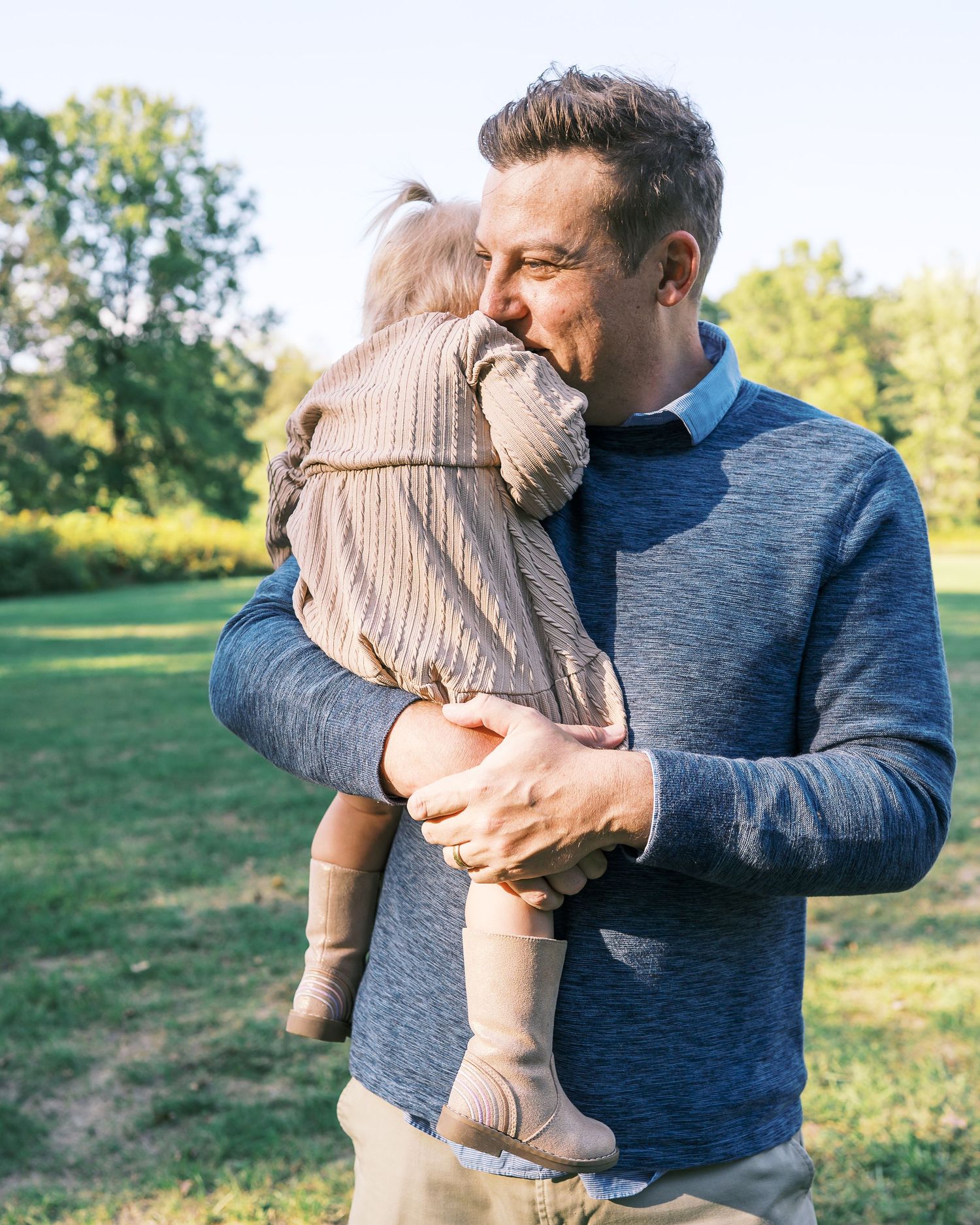 A warm embrace between two people wearing casual clothing in a sunny outdoor setting.