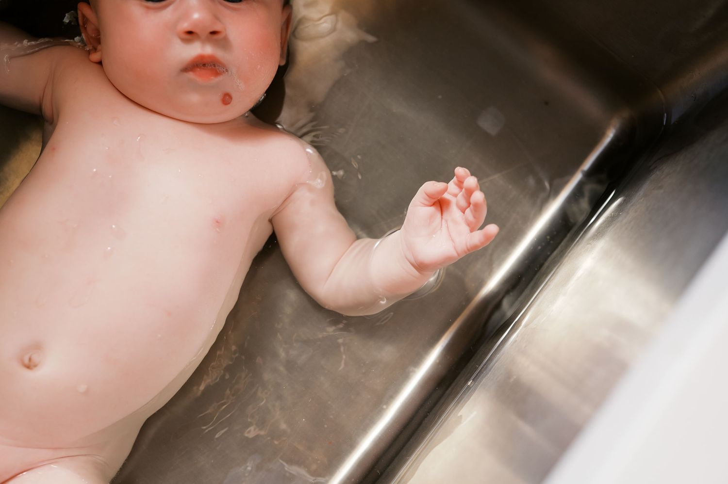 Close-up of baby exploring water during sink bath time.