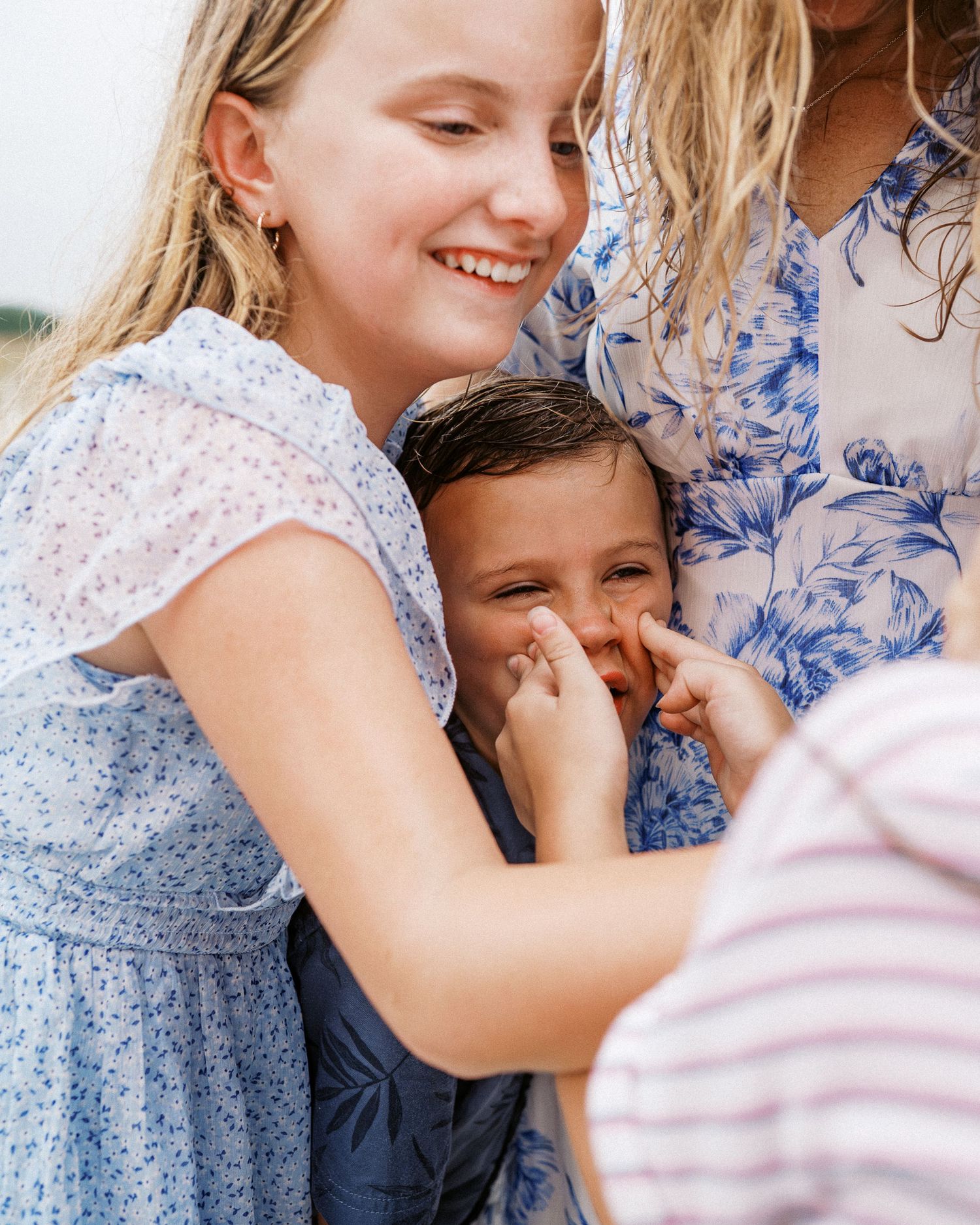 A joyful candid moment of laughter and smiles shared between people wearing blue and floral dresses outdoors.