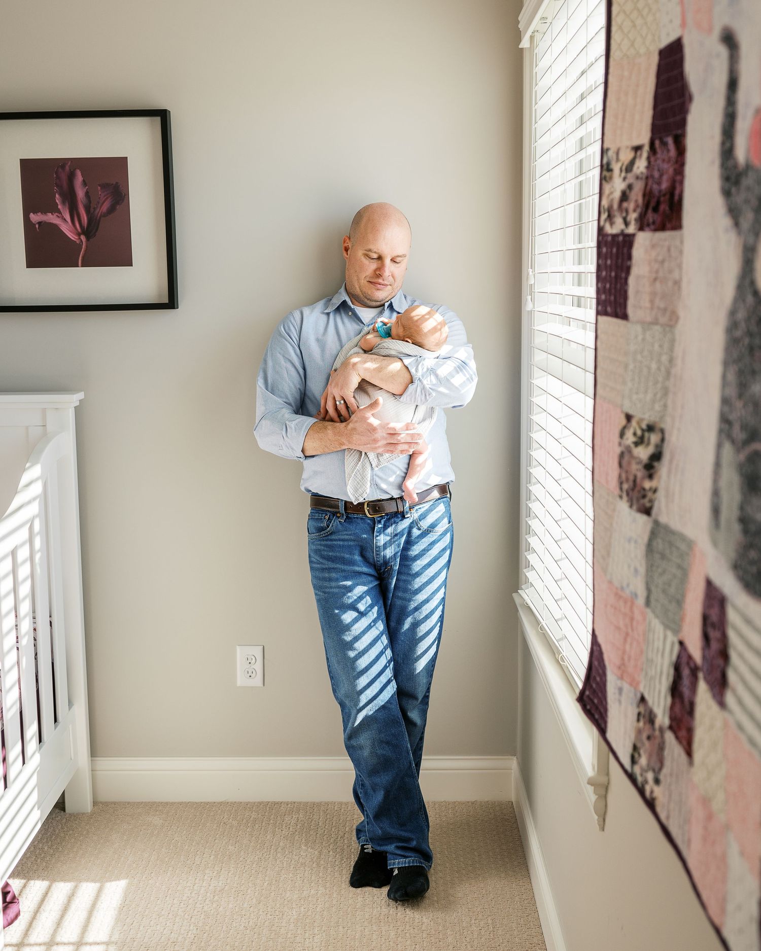Parent walking and holding newborn baby in sunlit room with art on walls.