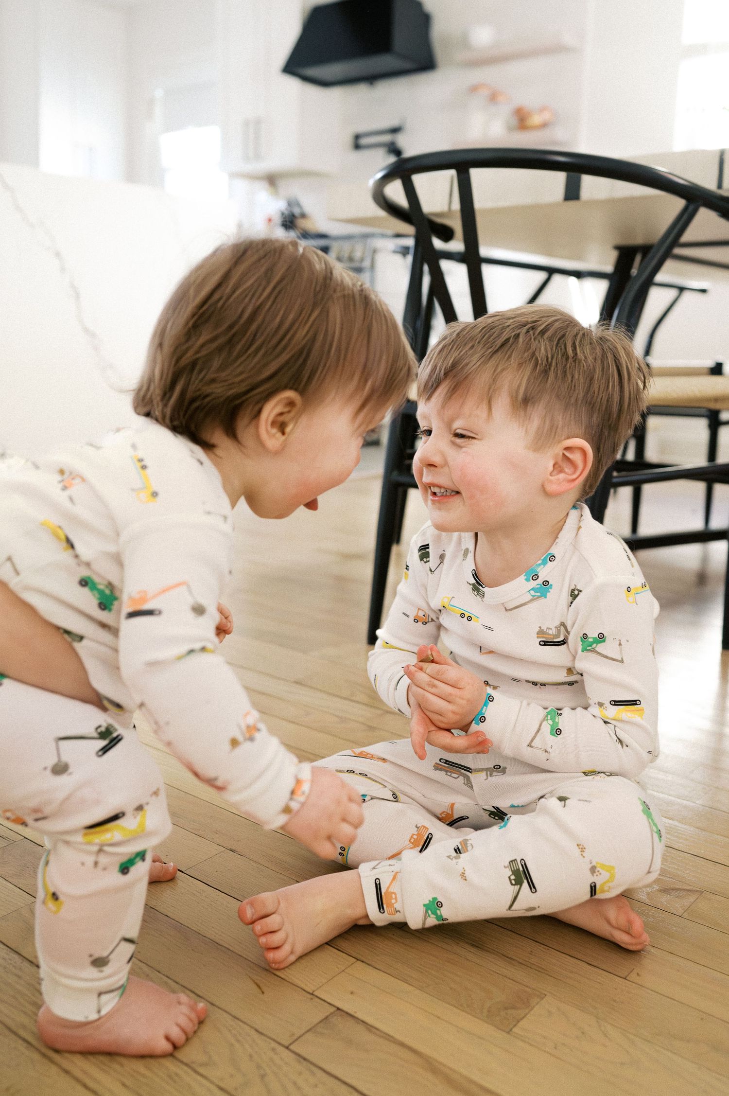 Children in matching white patterned outfits playing together on hardwood floors.