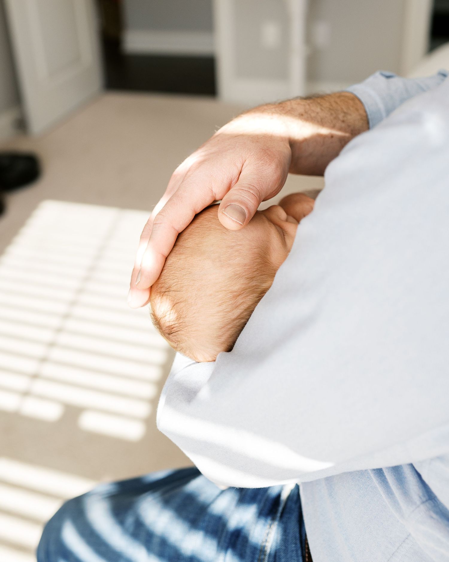 Close-up of hands gently holding a newborn baby in soft window light.
