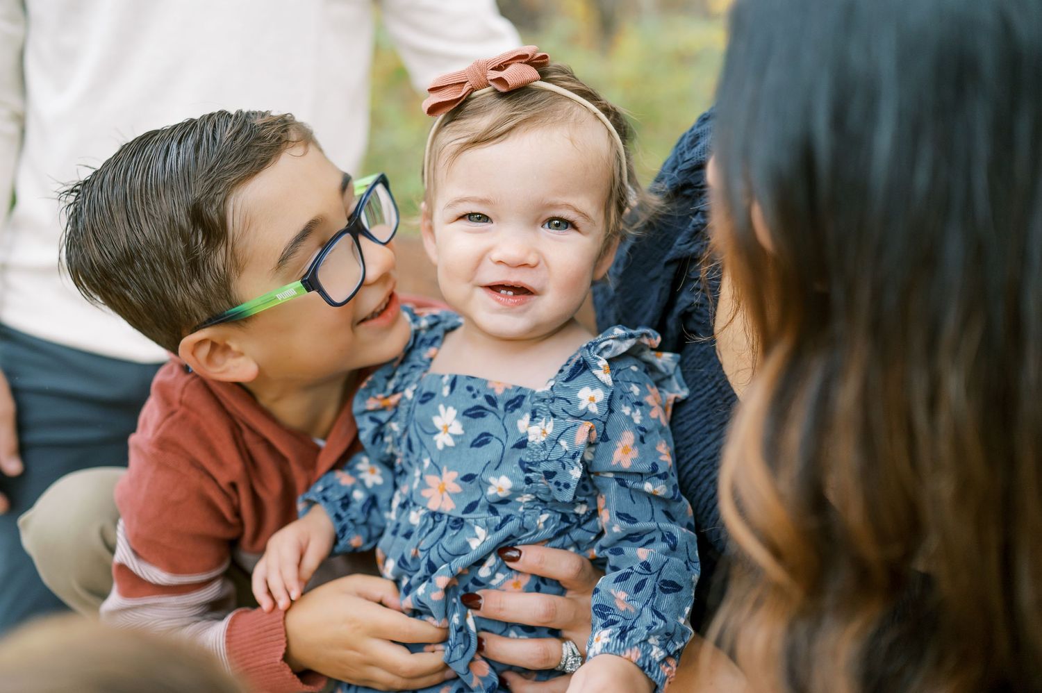Family shares intimate moment together during autumn photoshoot in park with yellow falling leaves.