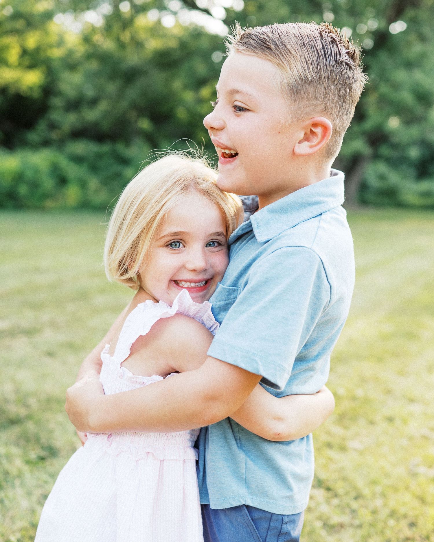Two children hugging and laughing together in a sunny green field.