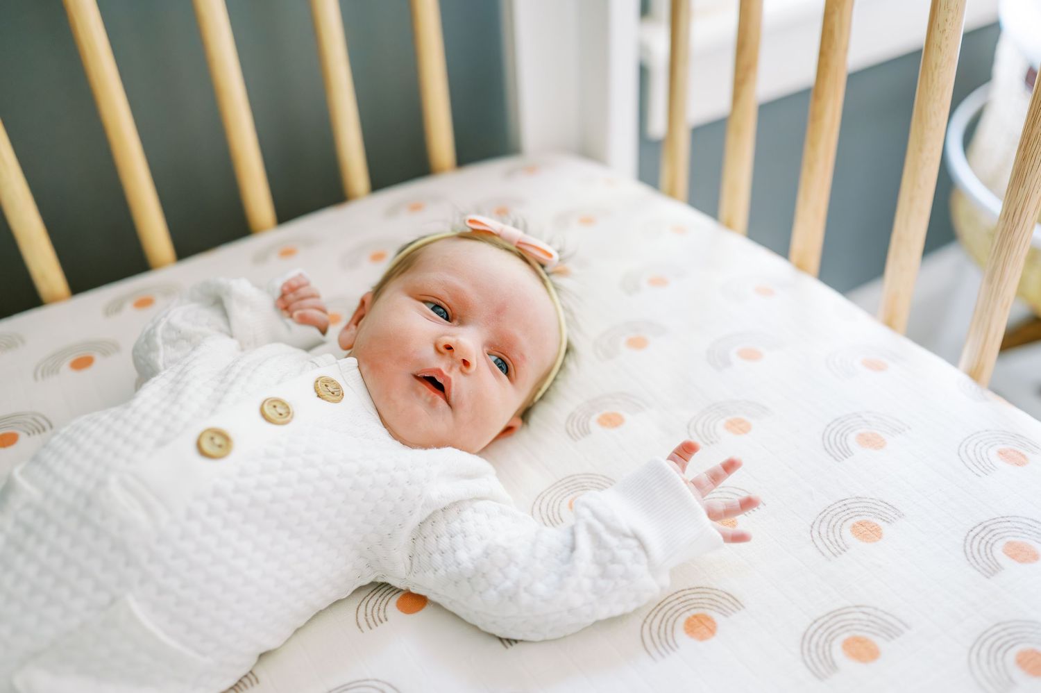 Baby resting on white polka dot bedding in wooden crib.