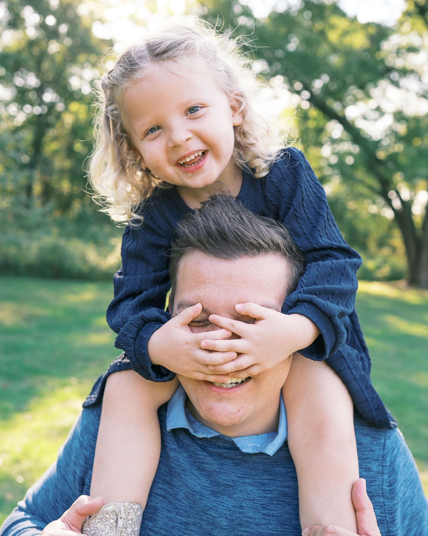 A playful moment between parent and child having fun outdoors on a sunny day in a grassy area.