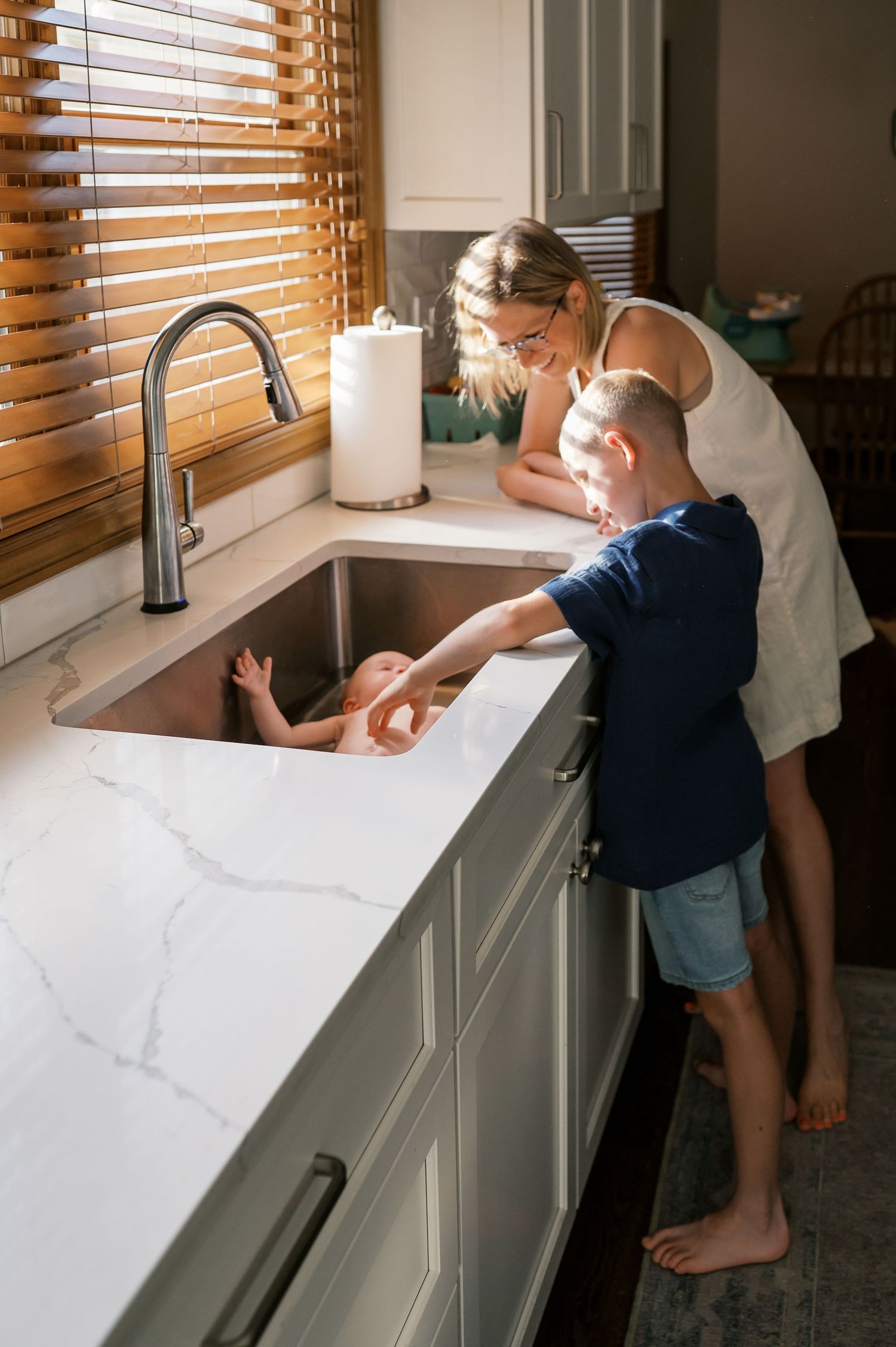 Family gathered around kitchen sink for baby's bath time routine.