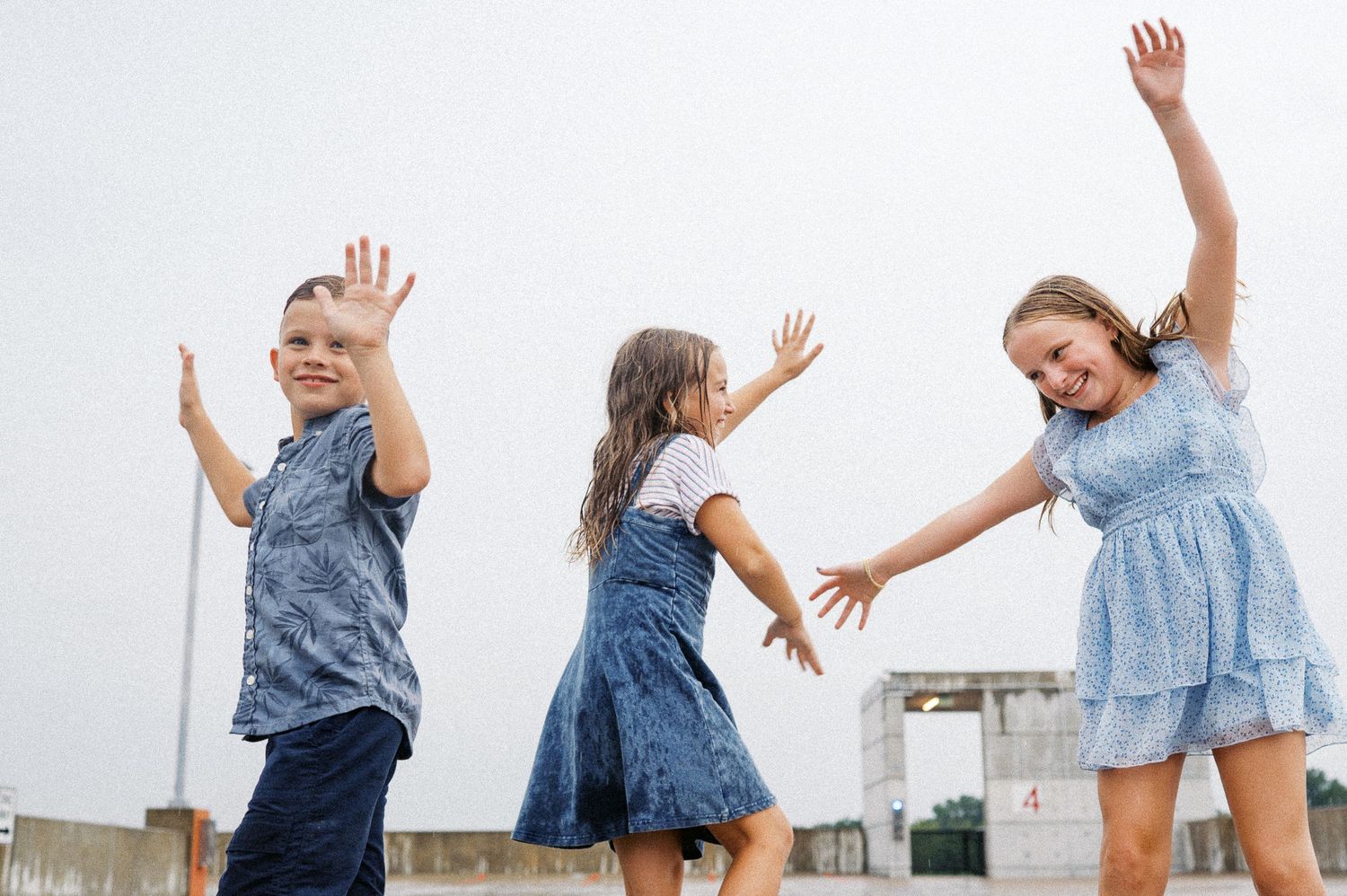 Three people jumping and playing together outdoors on an overcast day.