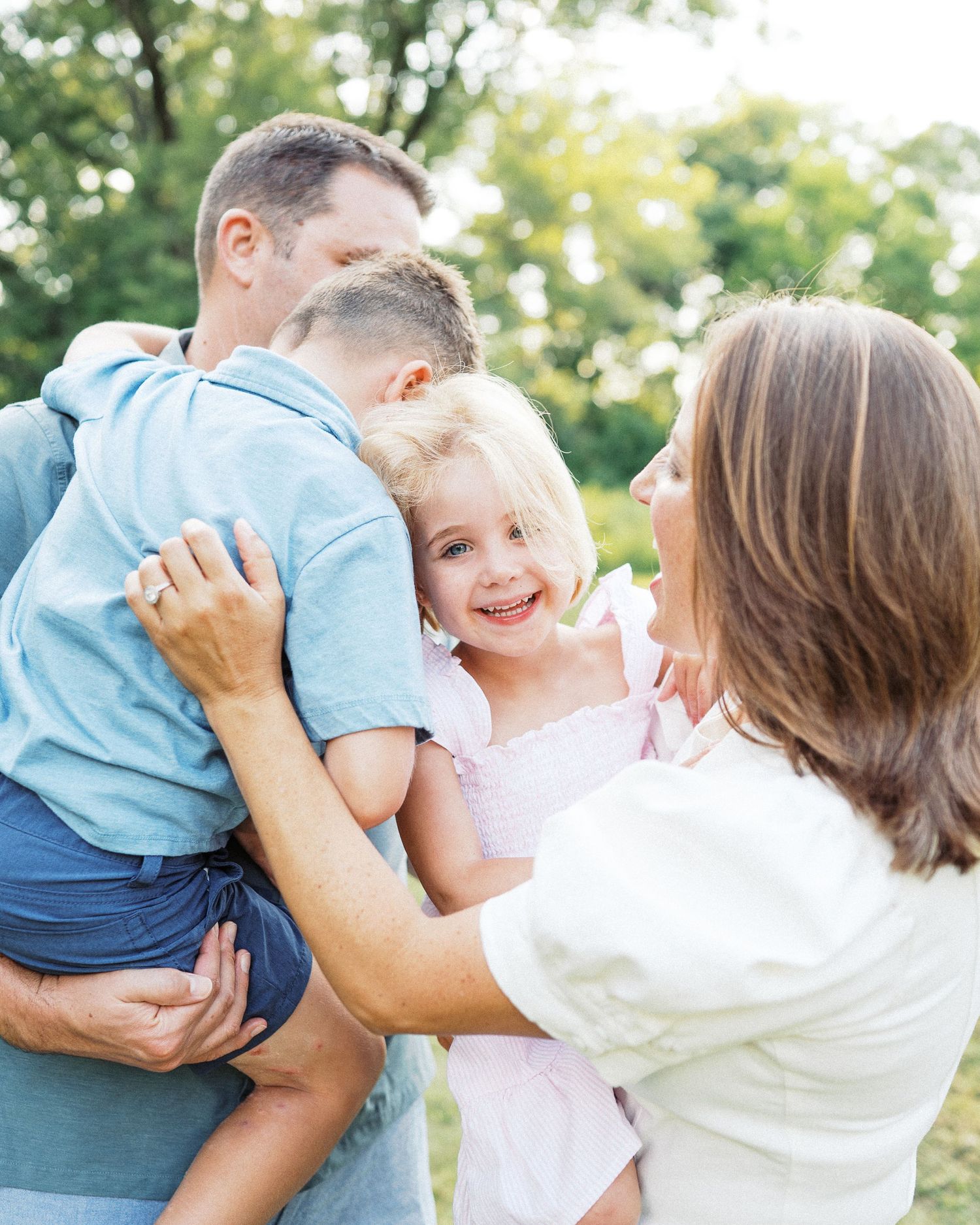 A family shares a tender outdoor moment together on a sunny day with greenery in the background.