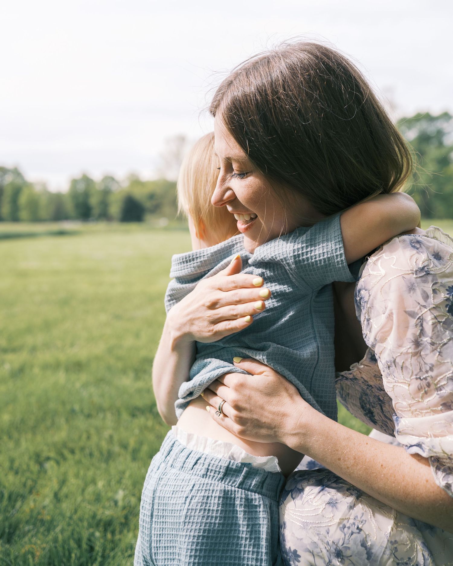 Mother hugging child in gingham outfit in sunny field.