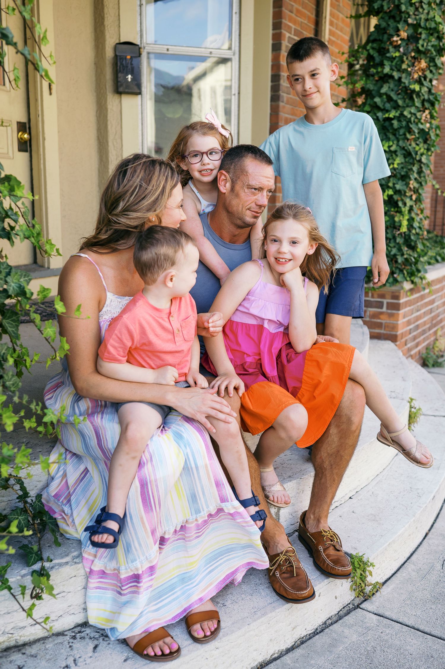 A family sits together on outdoor steps with greenery climbing the wall behind them.