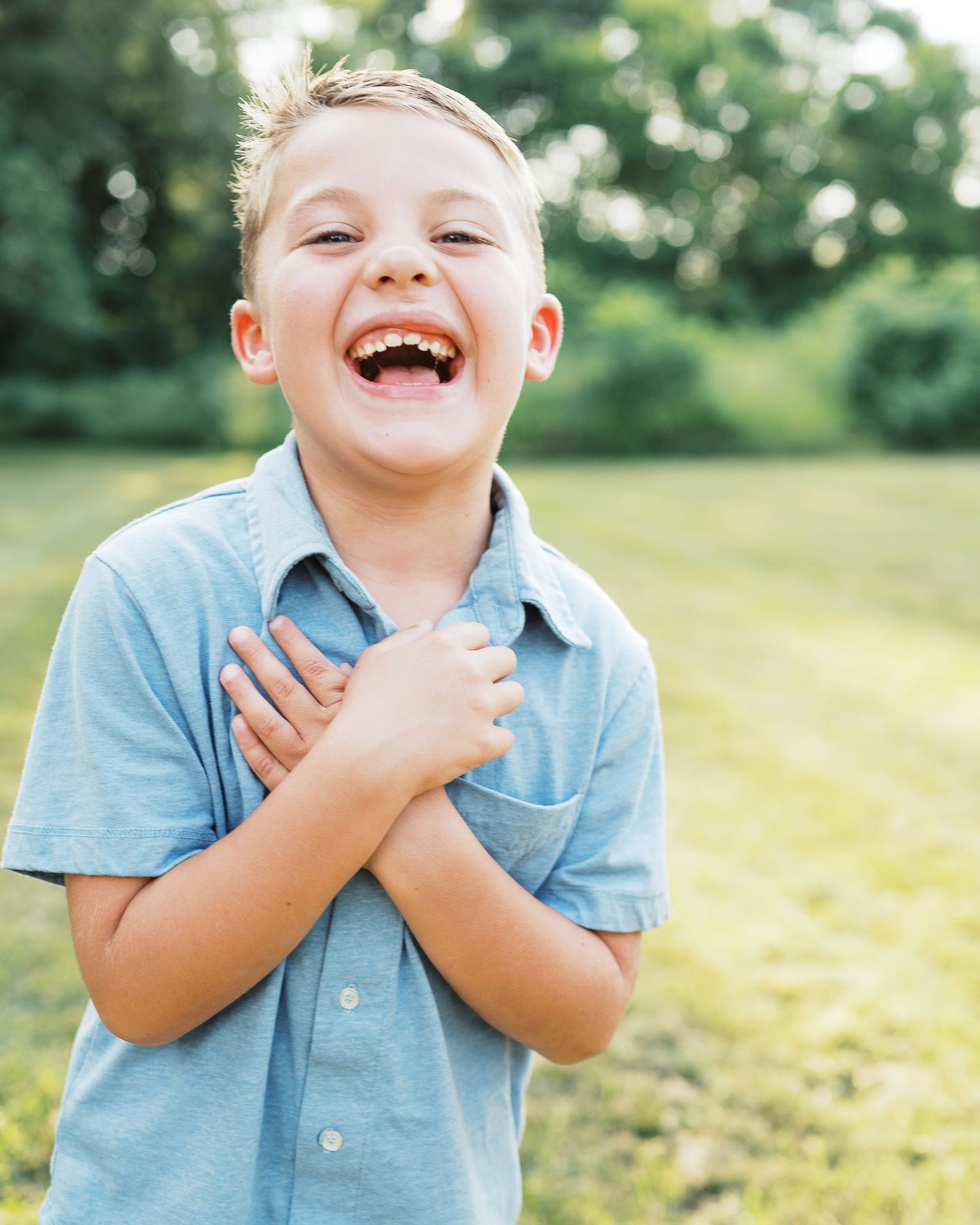 Young child in blue polo shirt laughing joyfully outdoors.