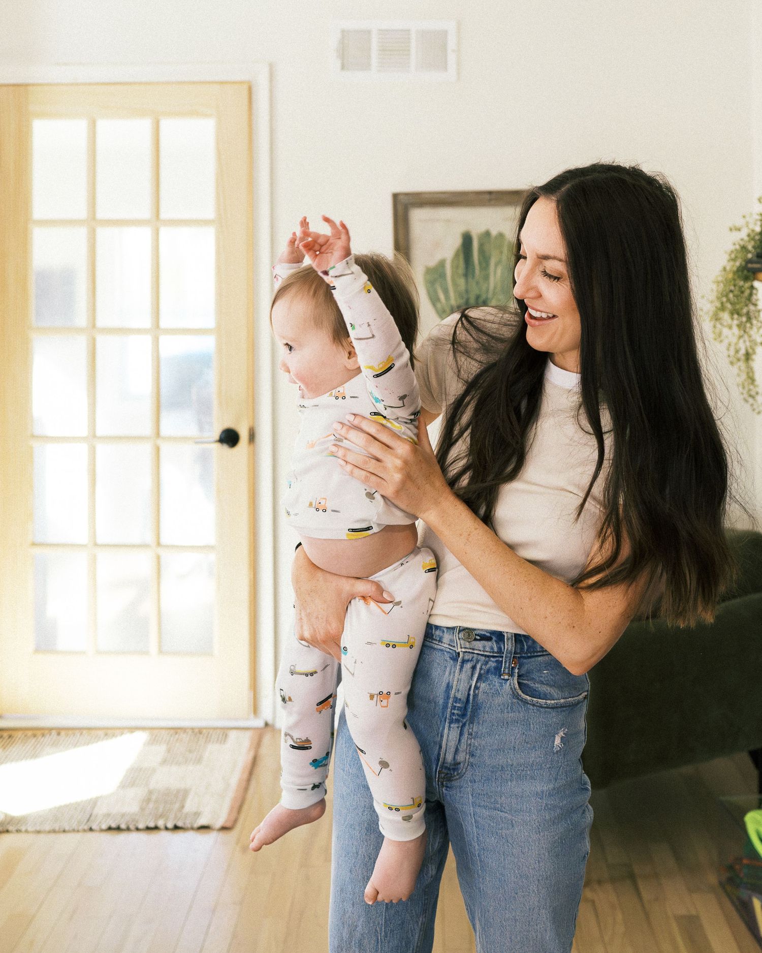 Mother and baby in matching printed pajamas share joyful moment by sunny window.