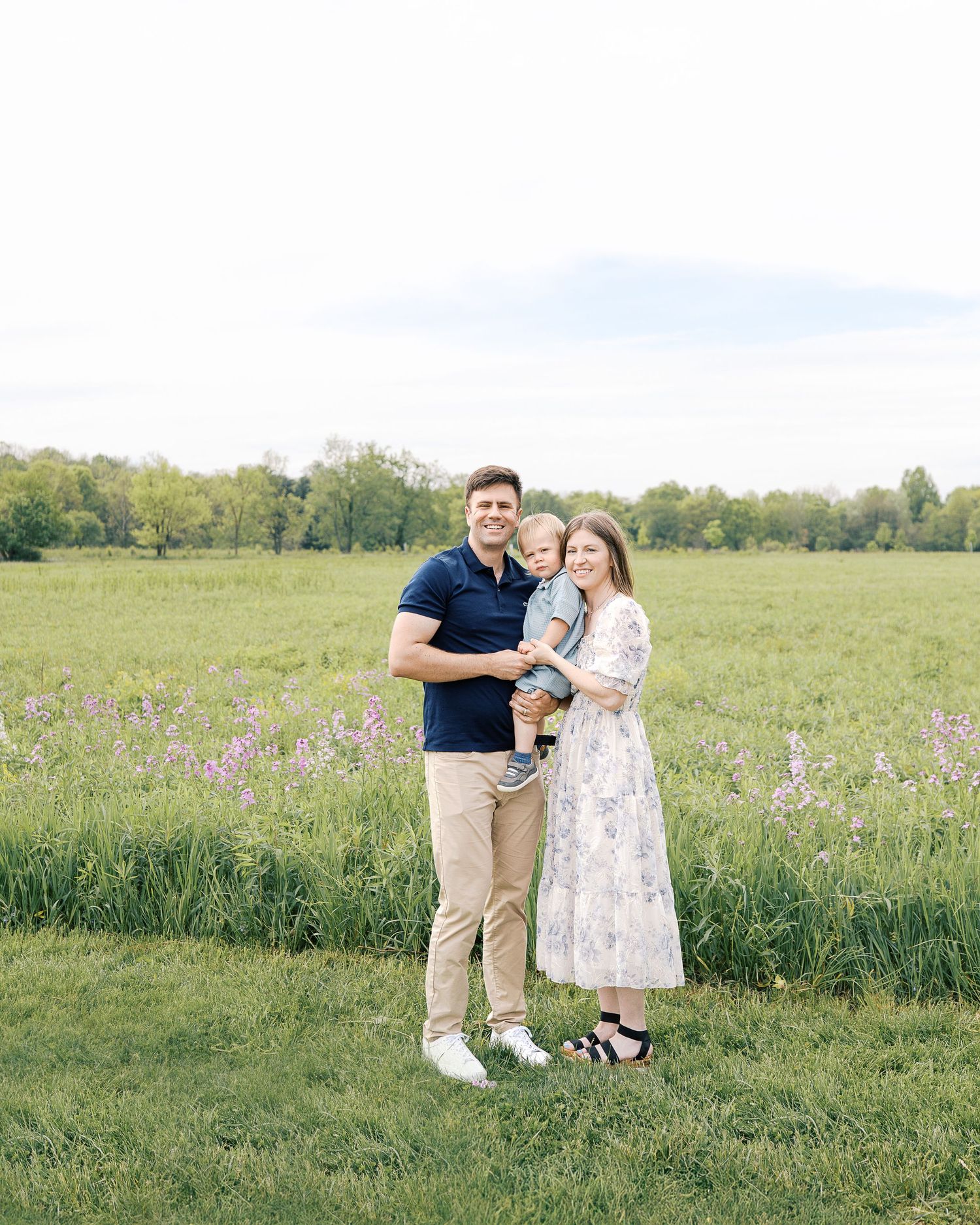 Family photoshoot in a vast green field with purple wildflowers during golden hour.