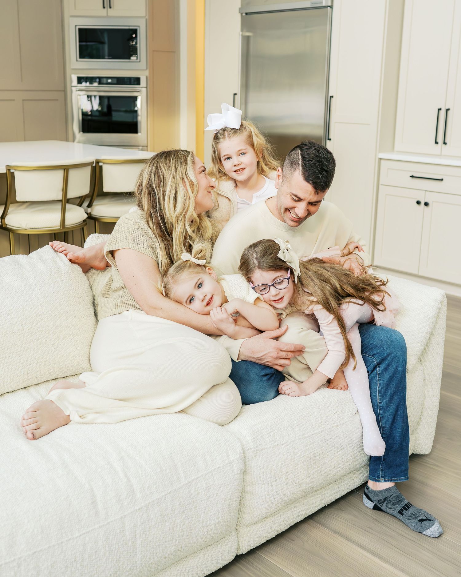 A playful family moment captured on a white couch in a bright modern kitchen setting.