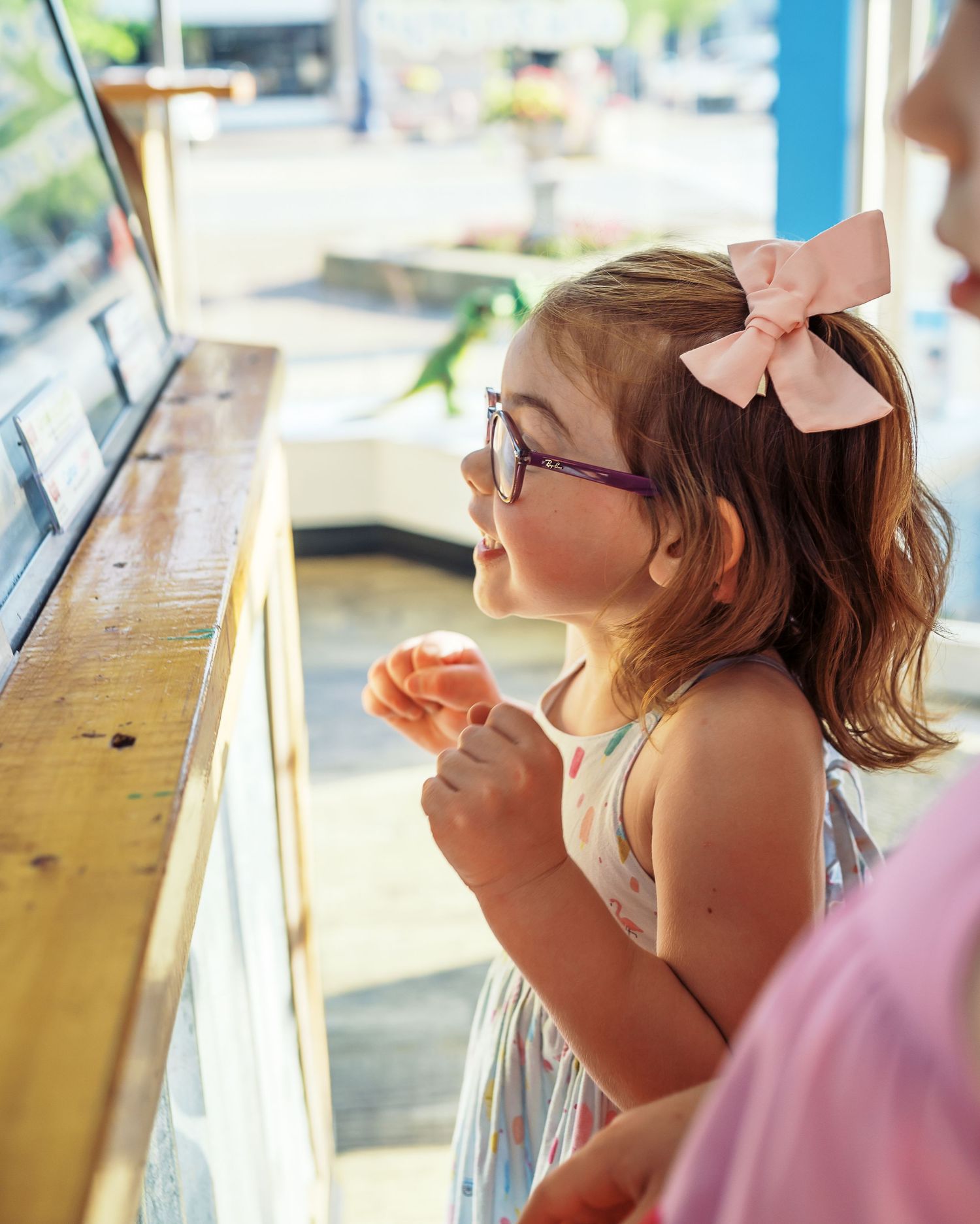 Child in glasses looking up at ice cream display case in sweet anticipation.