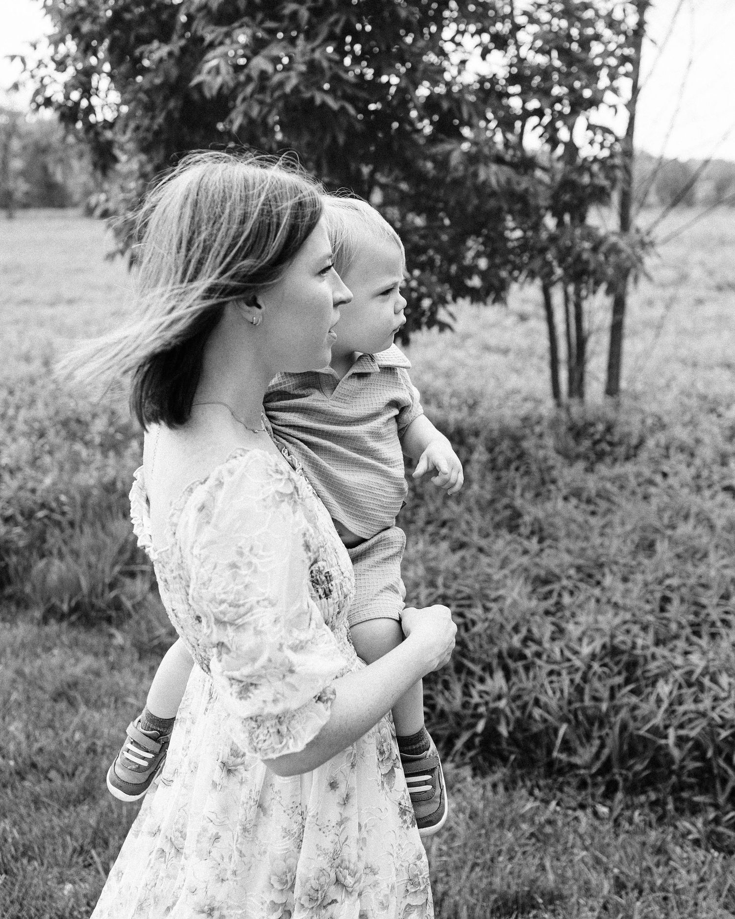 Black and white portrait of a child in a floral dress playing outdoors.
