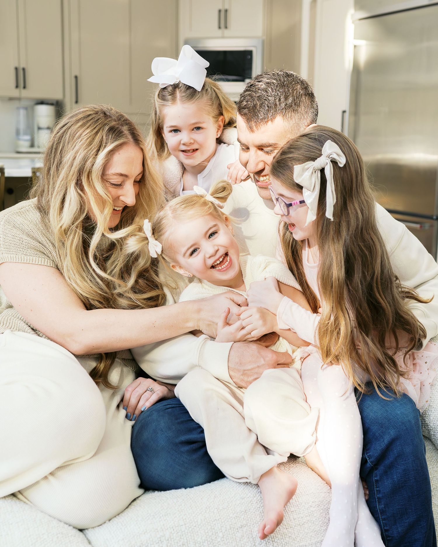 Candid family moments show joyful interactions on a white couch in natural light.