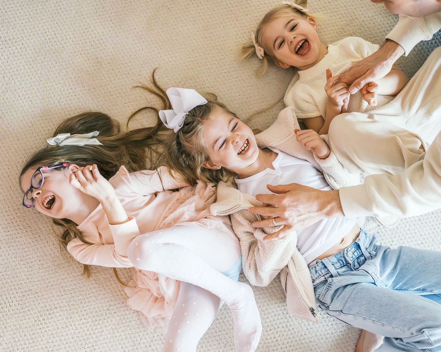 Candid moments of sisterly bonding on light carpet in natural lighting.