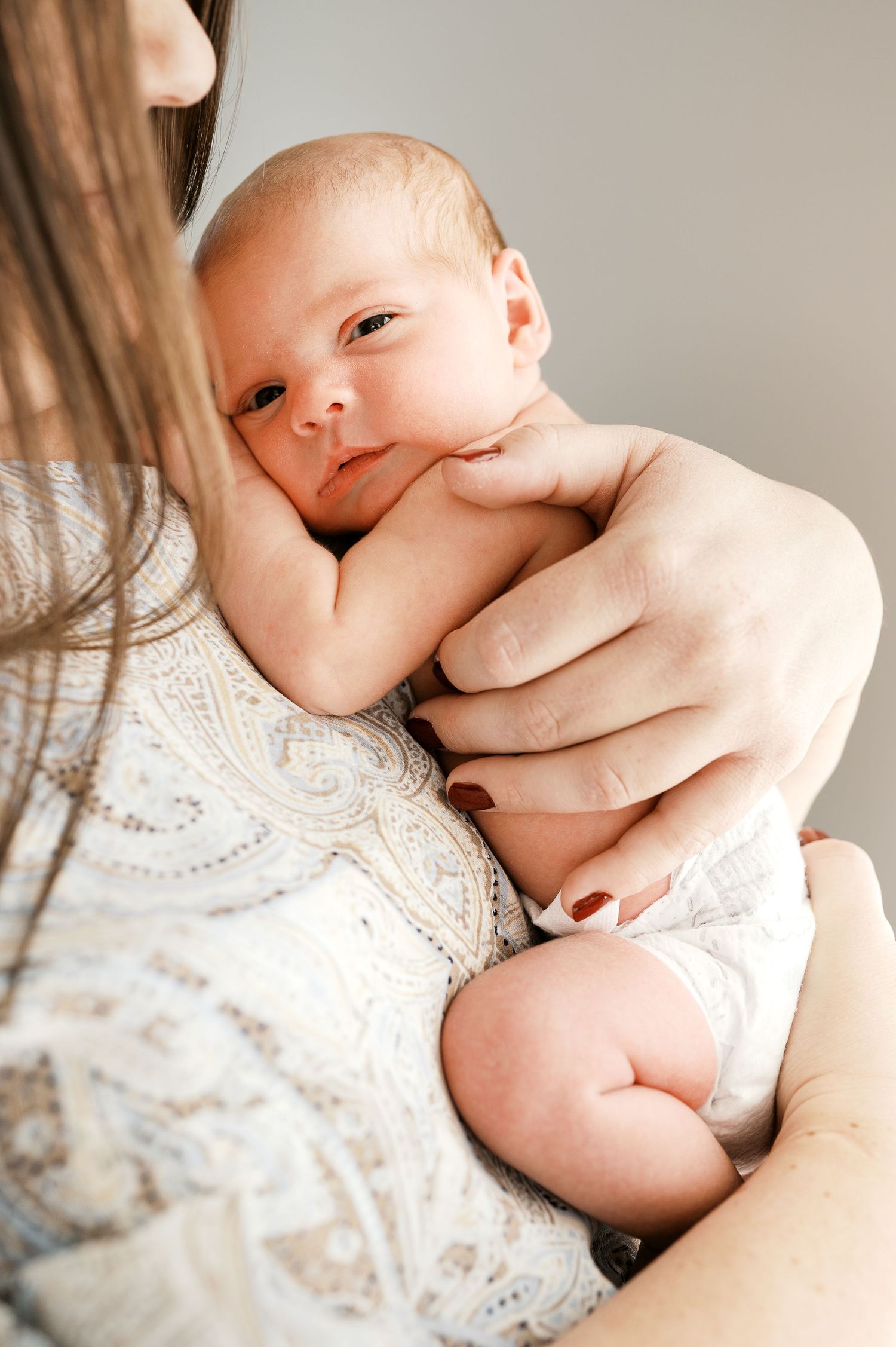 Close-up of a sleepy newborn baby being cradled against a lace-patterned garment.