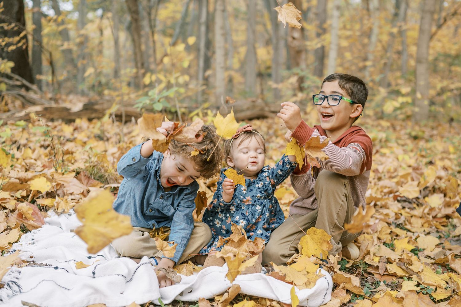 A family plays together in autumn leaves on a wooden boardwalk during a fall photo session.