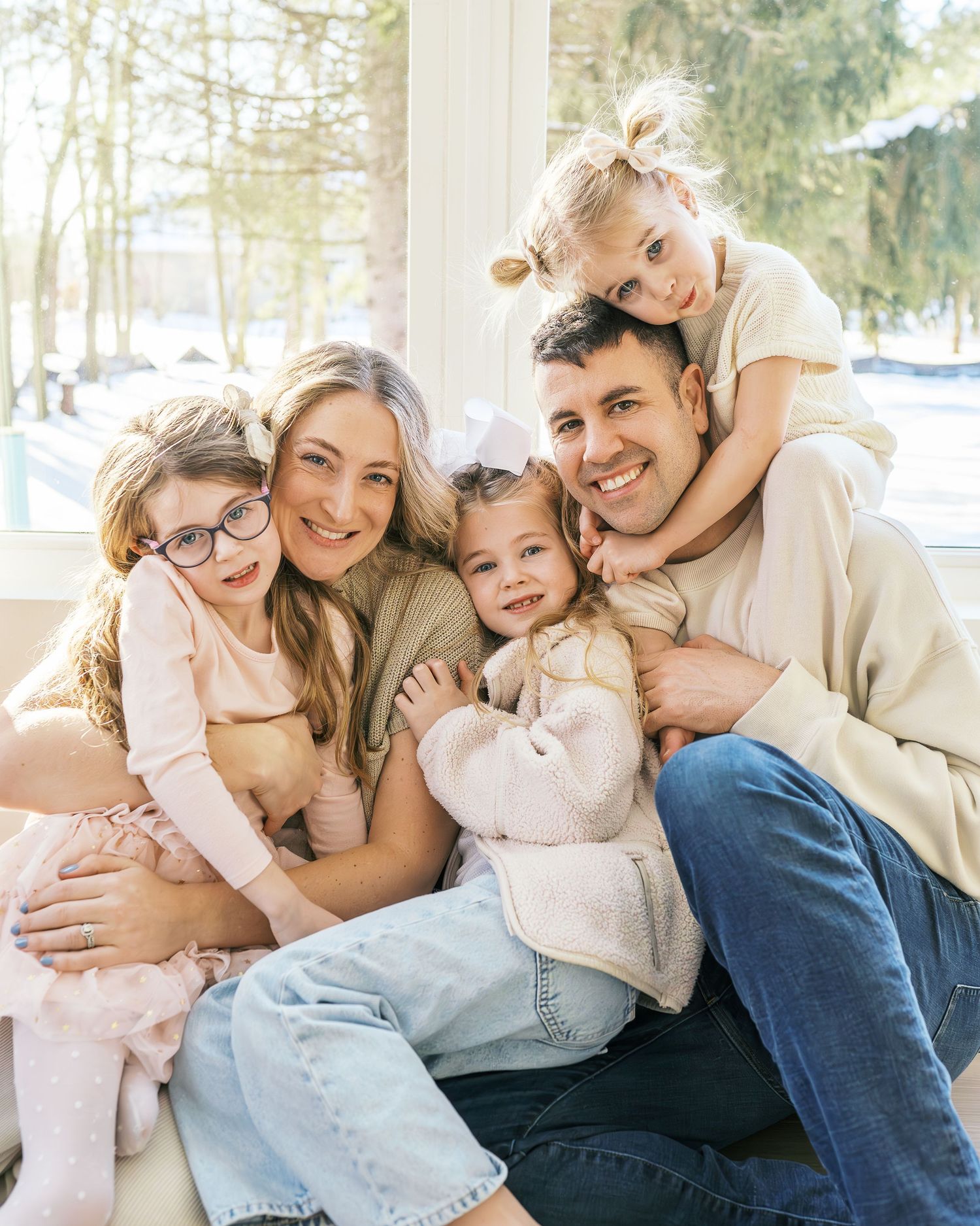 Candid shots of family playfully cuddling and laughing together by large windows.