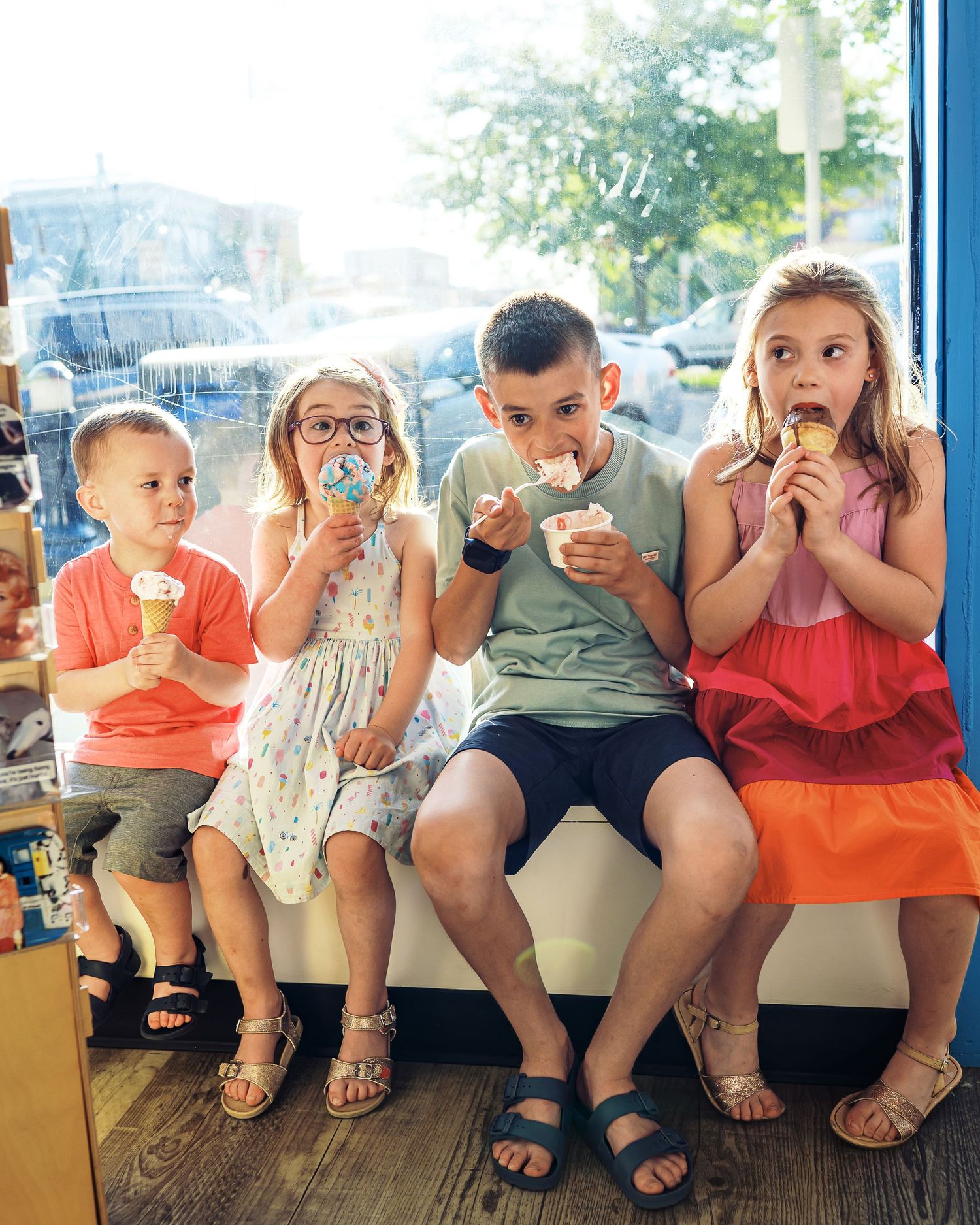Group of children sitting together enjoying ice cream cones on a sunny day.