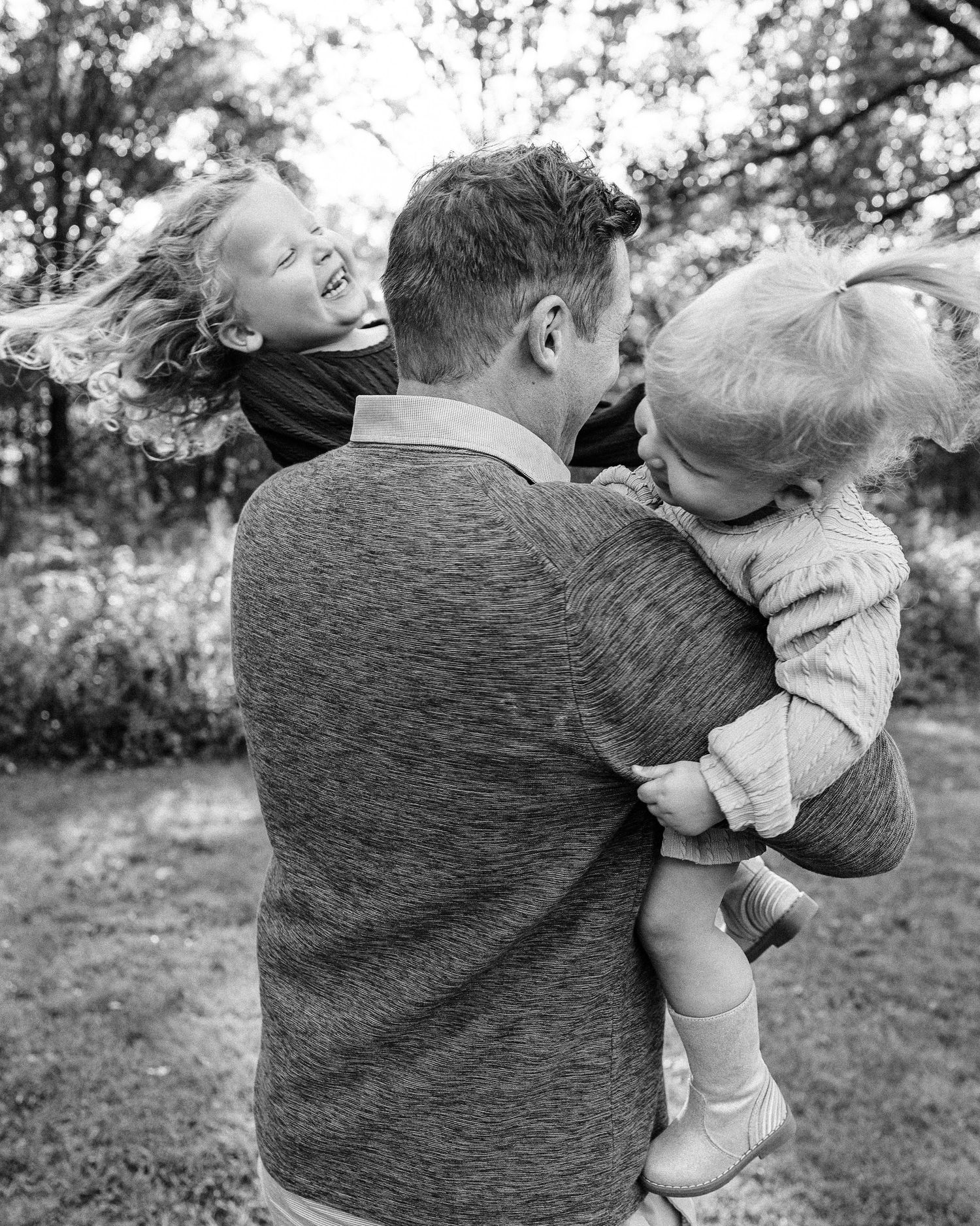 Black and white sequence of joyful outdoor playtime moments showing spinning and laughter in a natural setting.