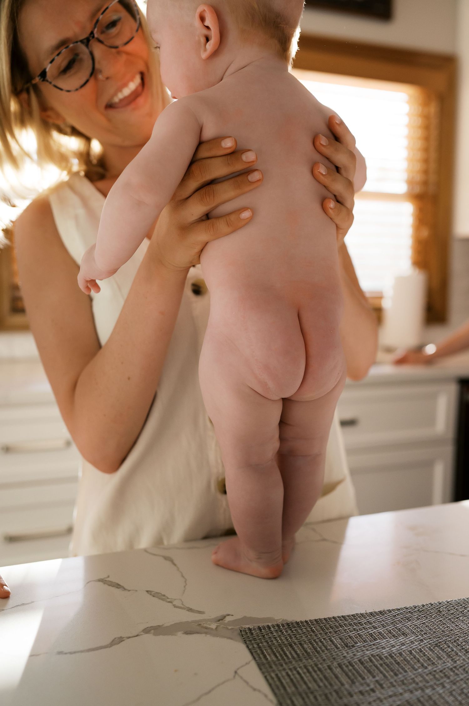 Baby bathing in kitchen sink while caregiver in white smiles and holds them securely.