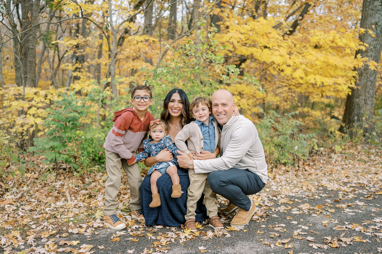 Family group photo session in park with beautiful yellow fall foliage in background.
