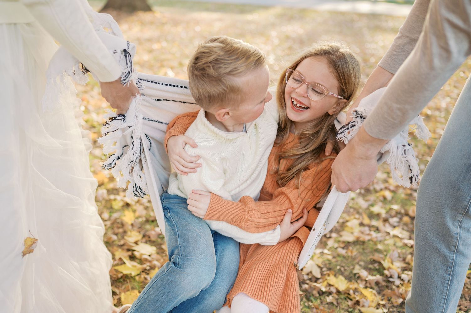 Two people playing and laughing together on fallen autumn leaves in a sunlit park setting.