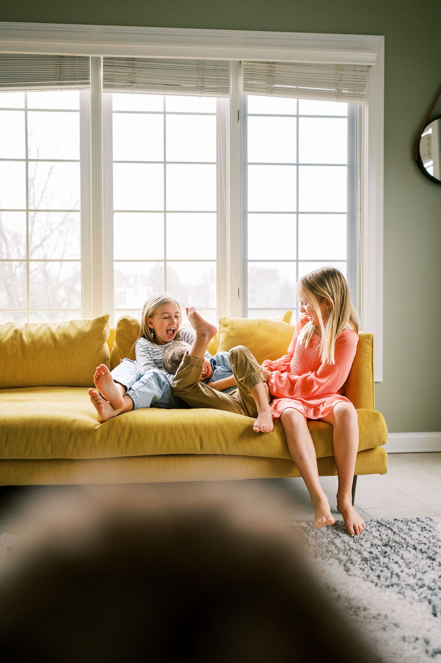 Family members lounging and playing on a yellow couch in a bright, modern living room.