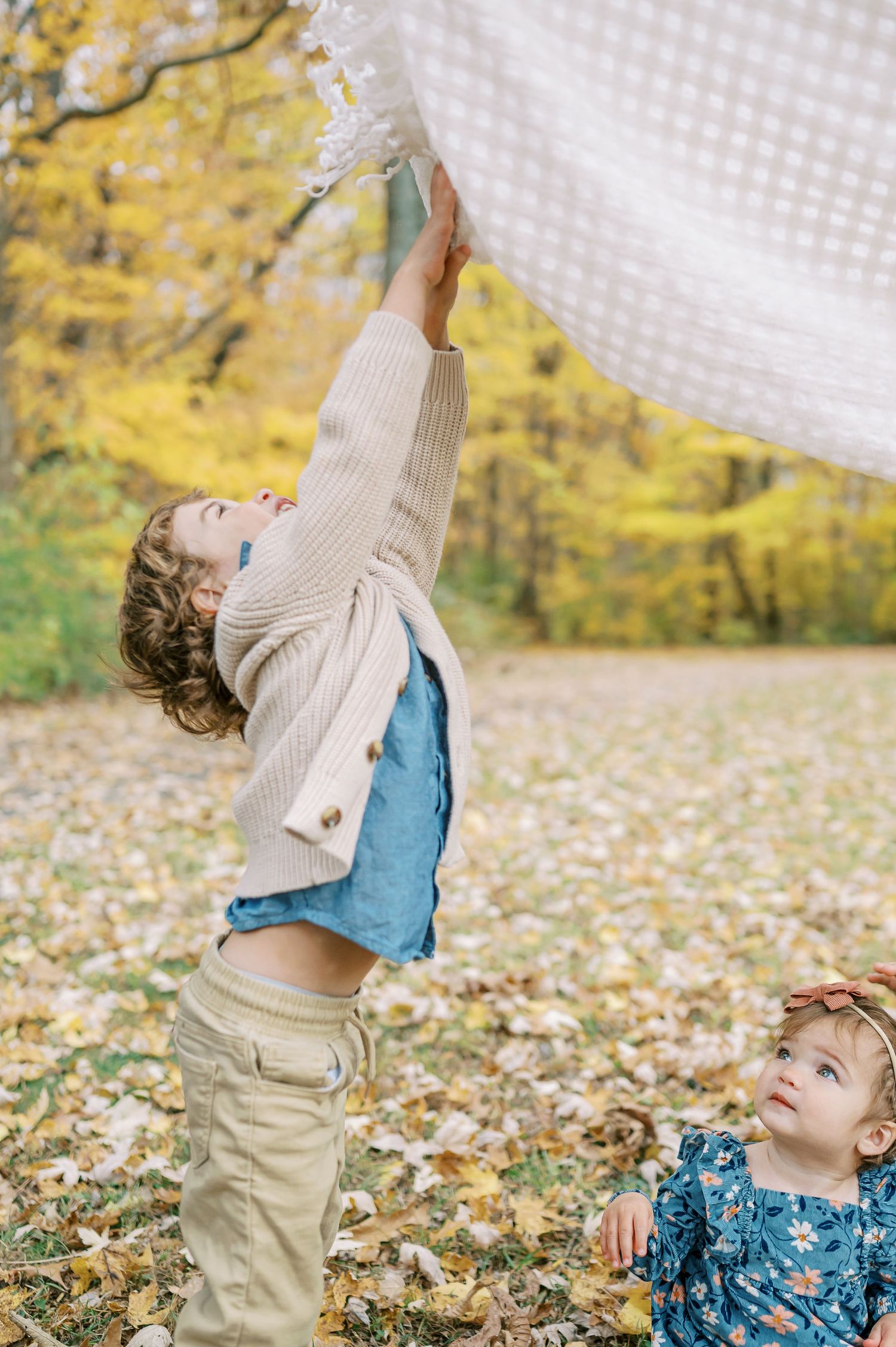 Children playing with white sheets outdoors against yellow fall foliage background.