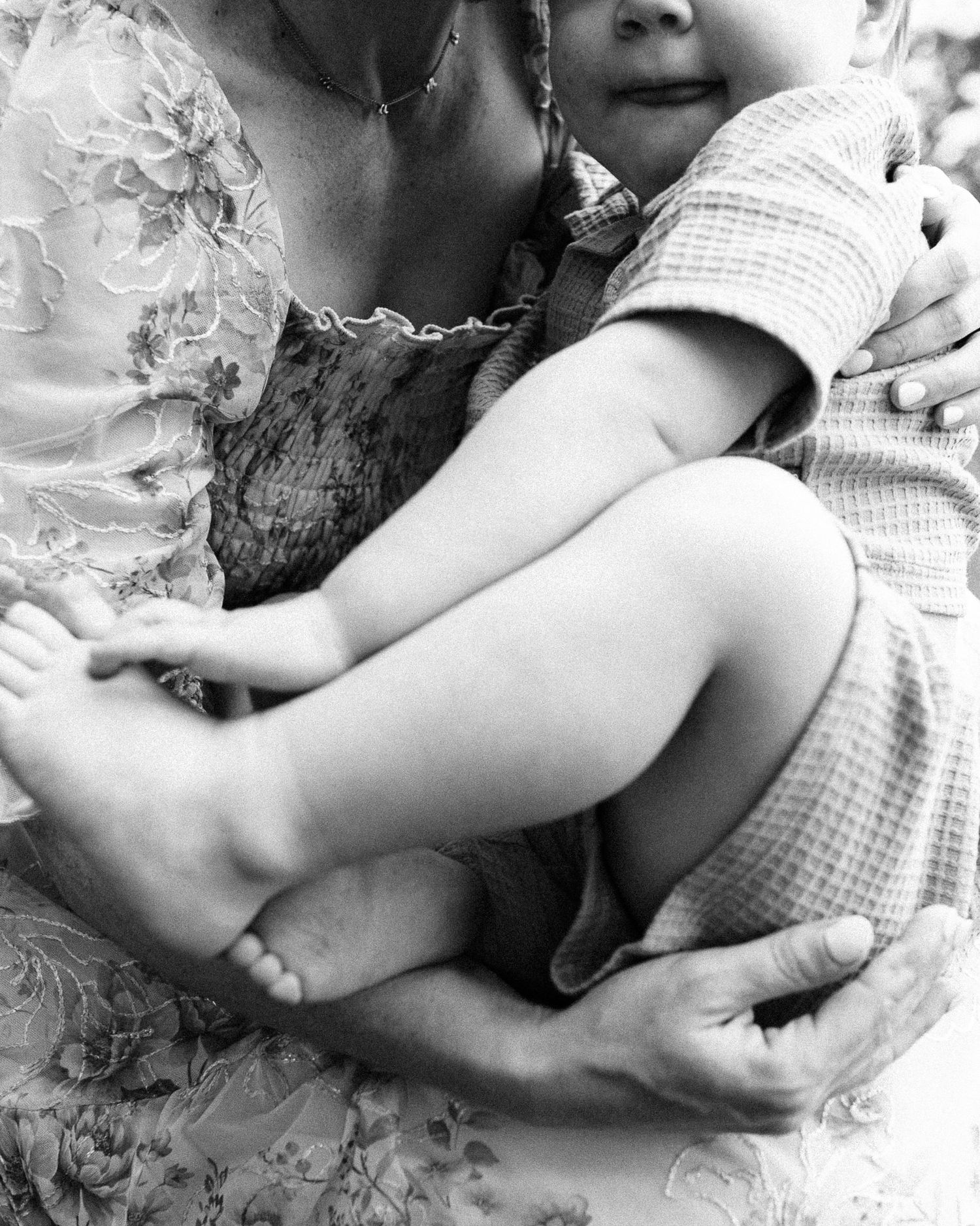 Close-up black and white image capturing intimate family cuddles on floral patterned fabric.