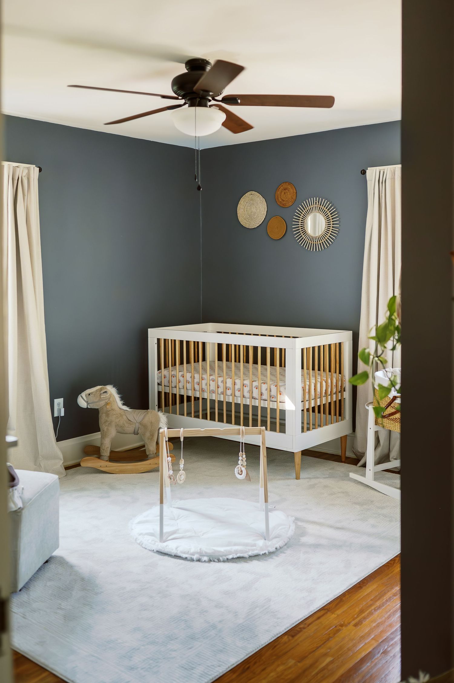 Modern nursery with white crib, gray walls, decorative plates, and a ceiling fan.
