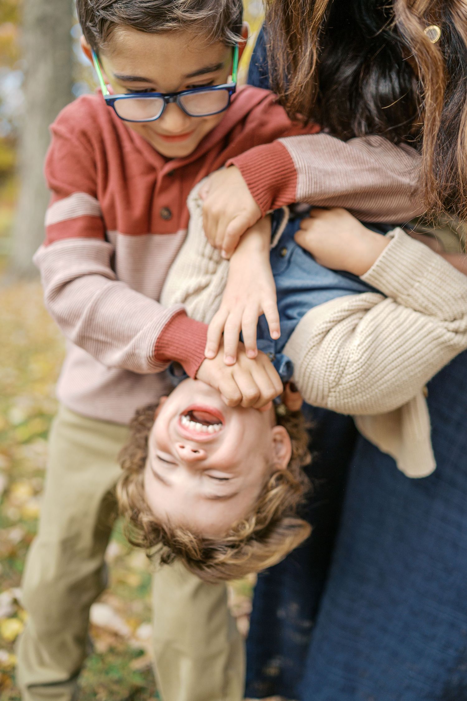 Playful family moment of holding child upside down outdoors in autumn.