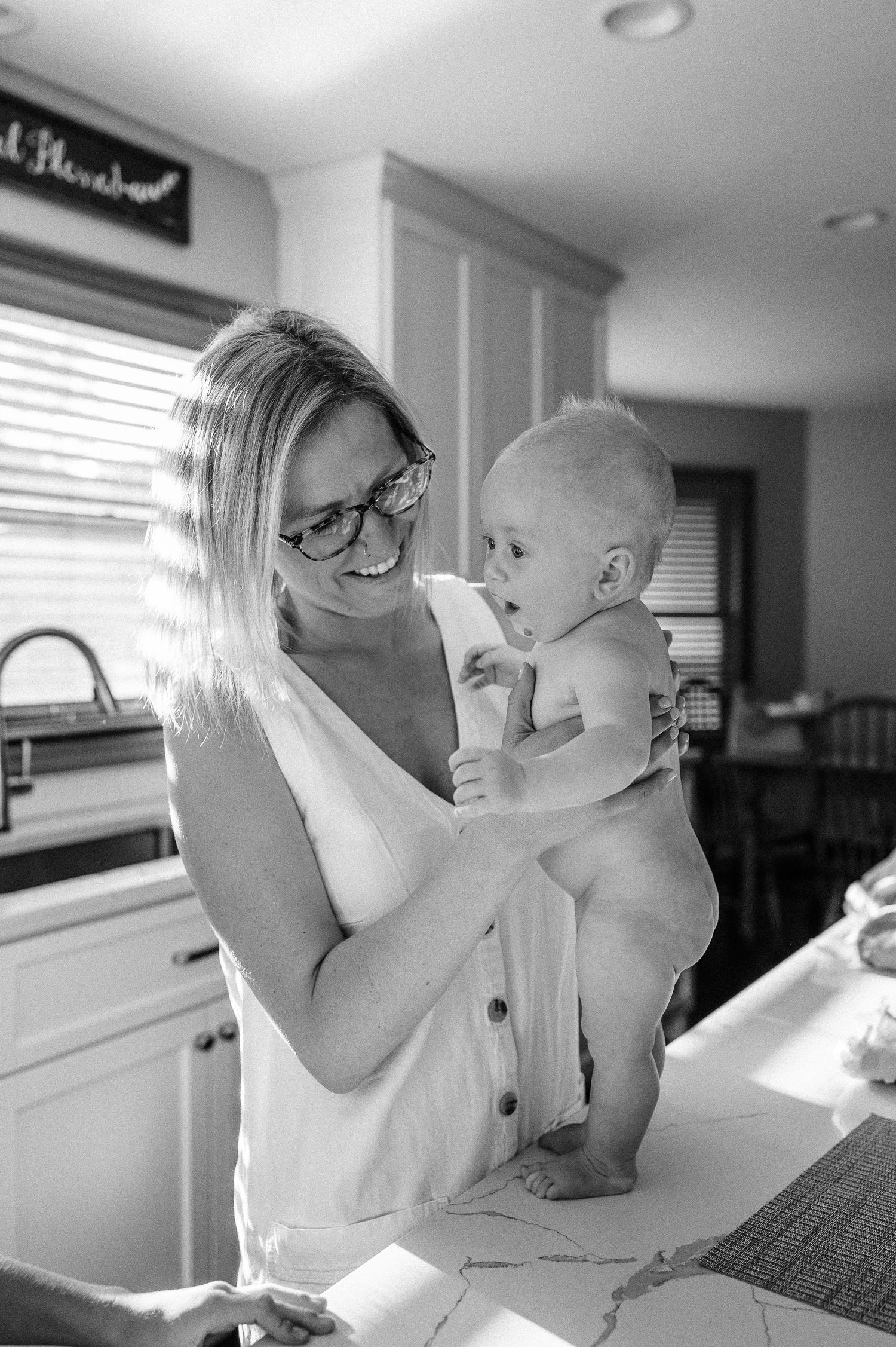 Tender moment as caregiver in glasses shares joyful interaction with baby during sink bath.