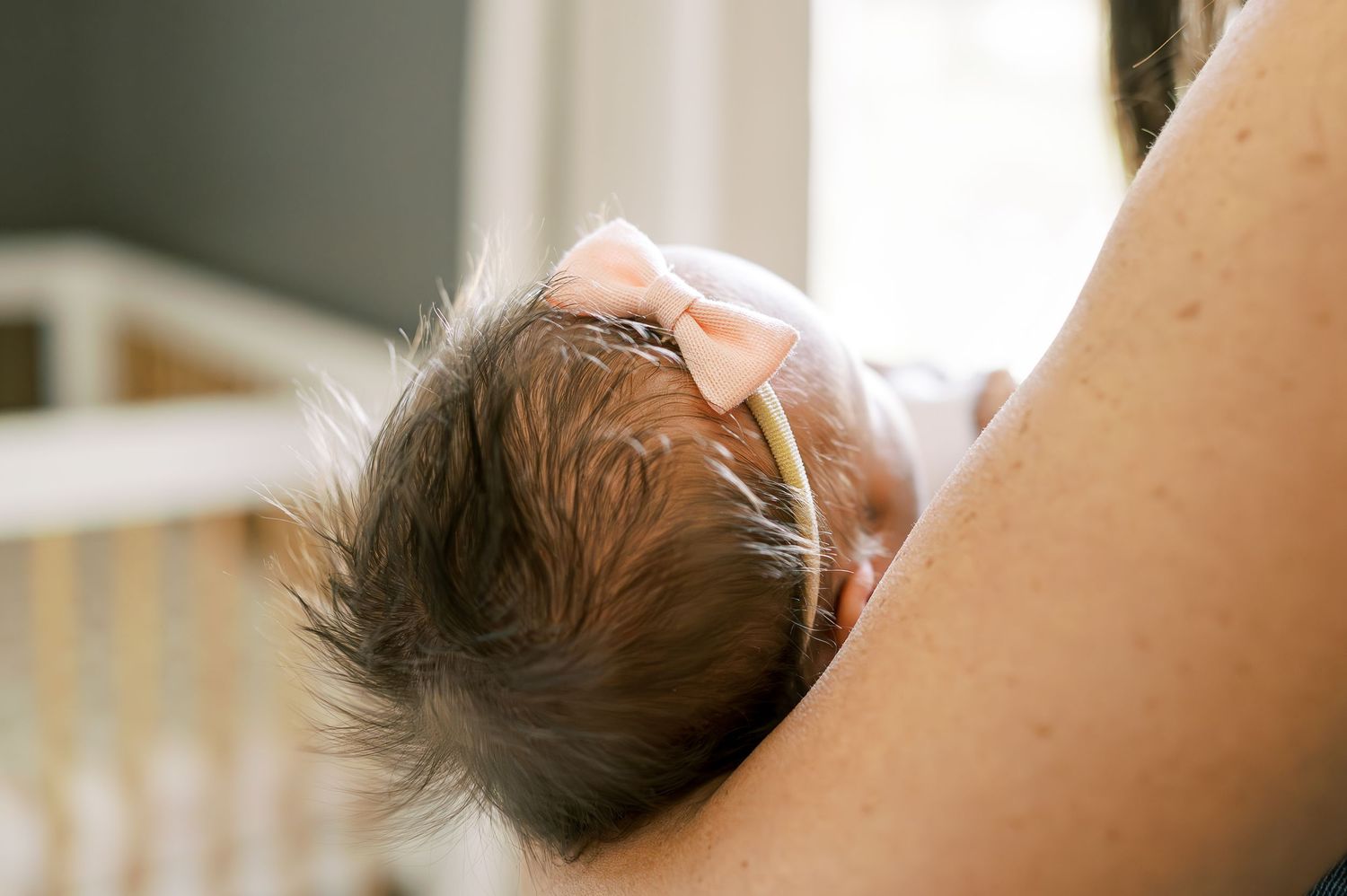Close-up view of a sleeping newborn with dark hair wearing a white headband.