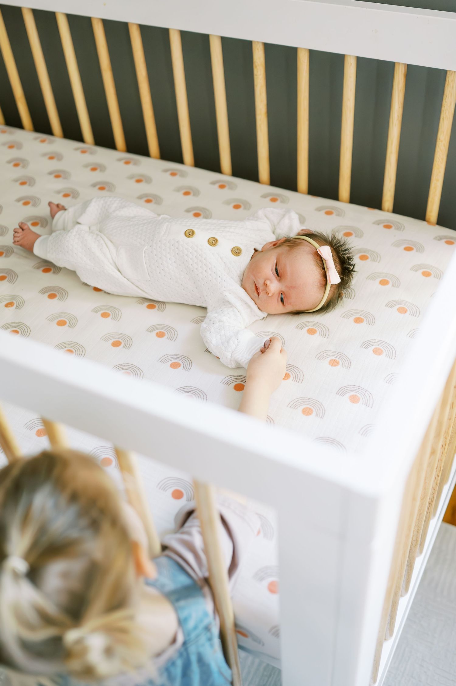 Baby resting in wooden crib with orange patterned bedding.